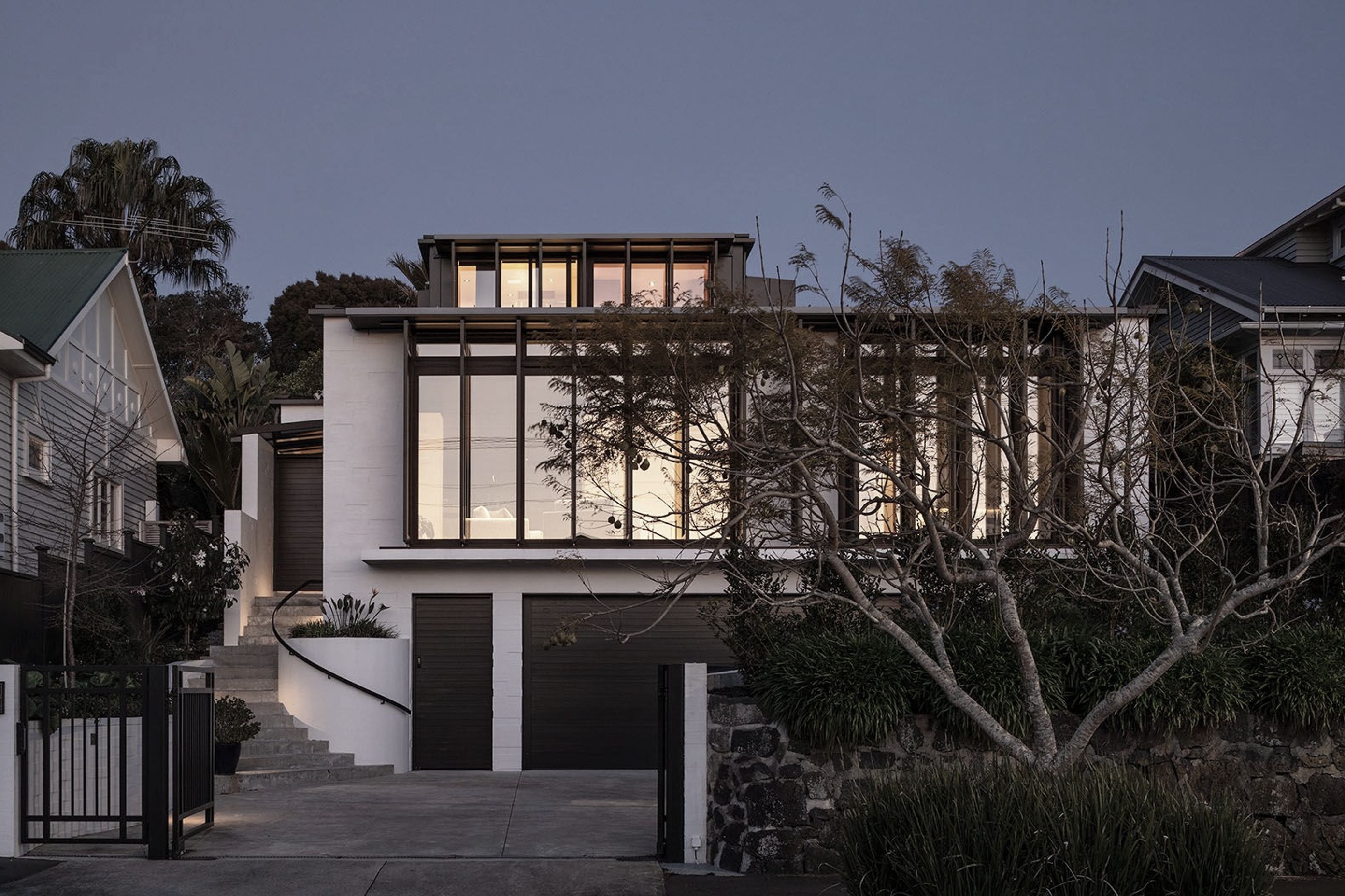 From the street, the western elevation rises across three clear levels—bagged concrete blocks are punctuated with floor-to-ceiling glazing on both the second and third storeys