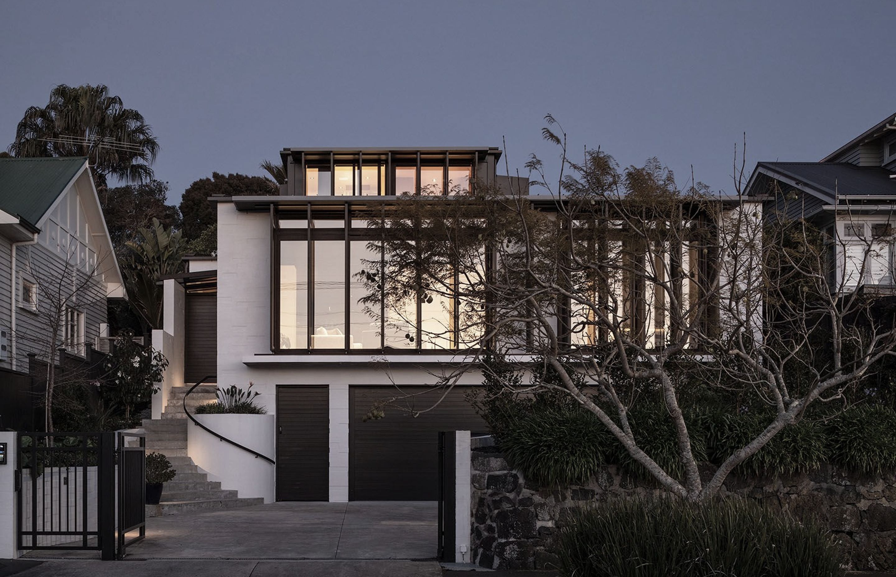 From the street, the western elevation rises across three clear levels—bagged concrete blocks are punctuated with floor-to-ceiling glazing on both the second and third storeys