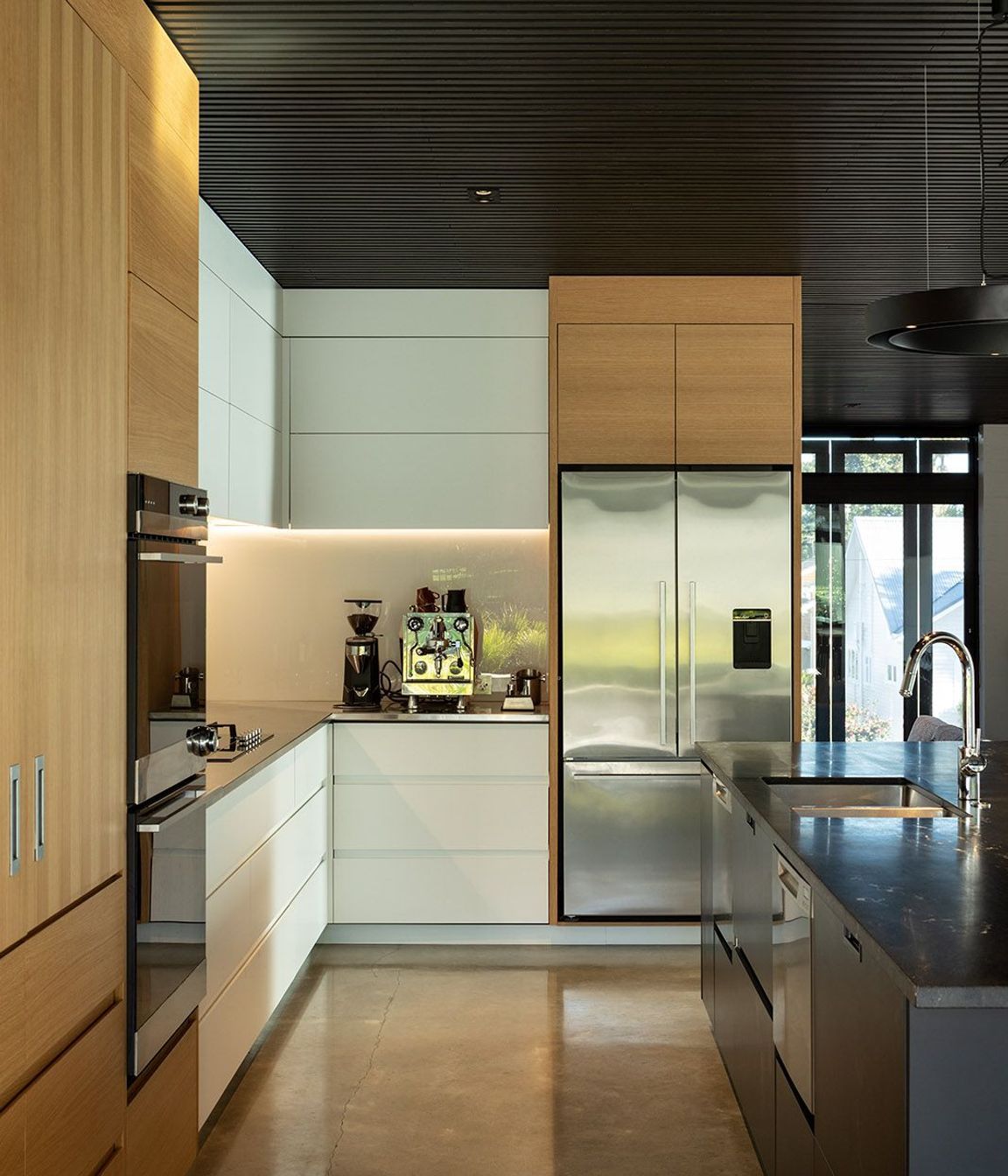 The dark cedar ceiling is complemented by a polished concrete floor, white oak veneer cabinetry and a dark grantie benchtop.