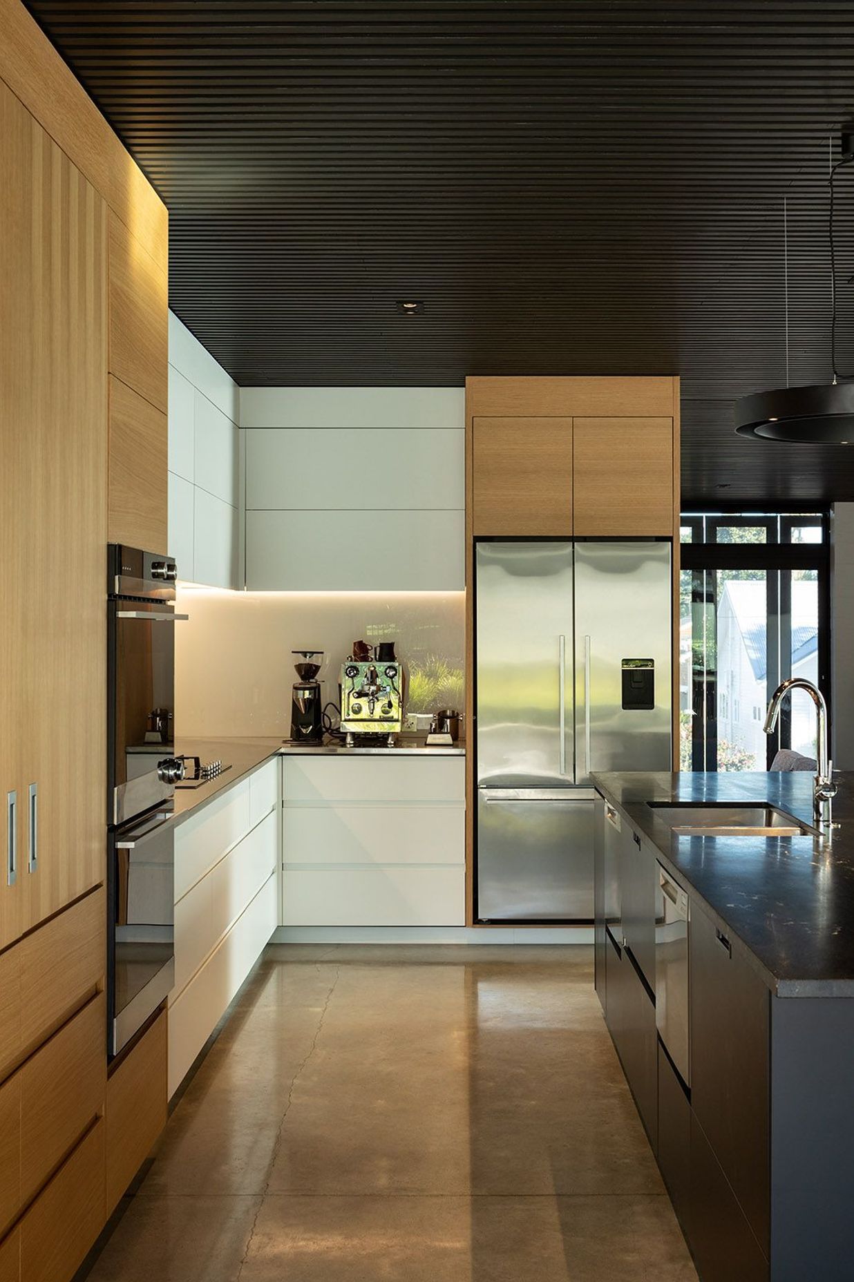 The dark cedar ceiling is complemented by a polished concrete floor, white oak veneer cabinetry and a dark grantie benchtop.