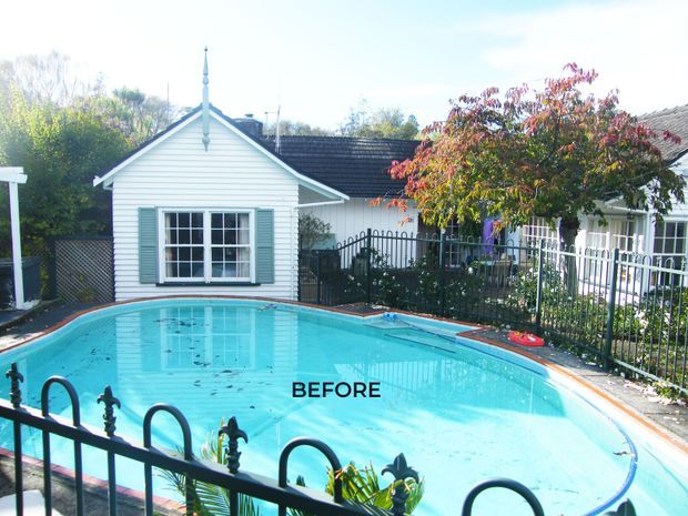 A bright exterior view of a residential swimming pool in front of a small white weatherboard outbuilding with a gabled roof, decorative finial, and green shutters. Black metal fencing surrounds the pool, with a larger light-coloured house partially visible behind it. The image is labelled “BEFORE,” suggesting a renovation or landscaping comparison.