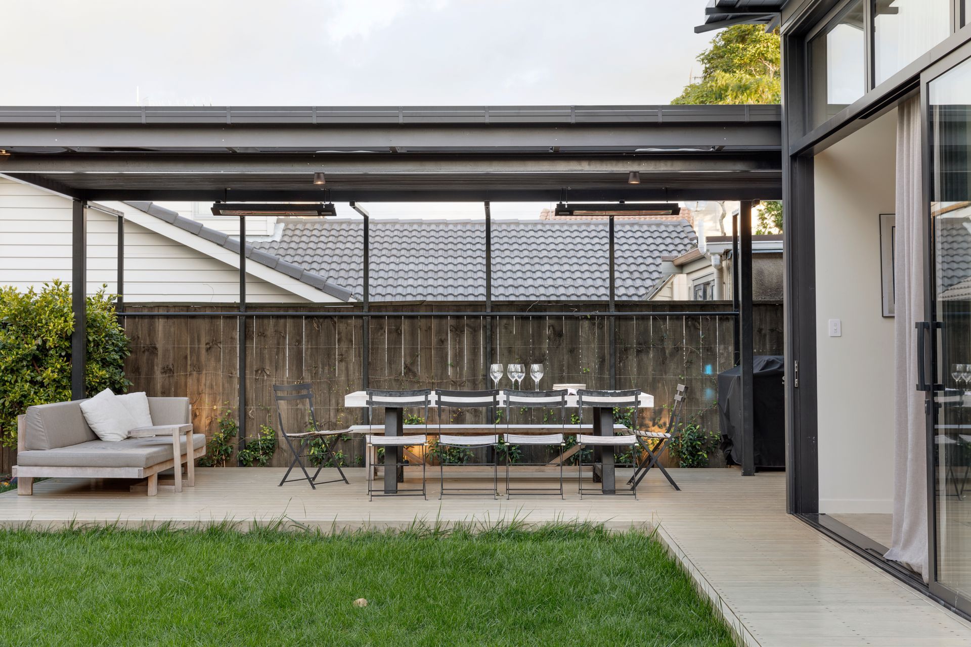 The dark-stained pergola provides a covered outdoor dining and lounge area off the indoor kitchen.