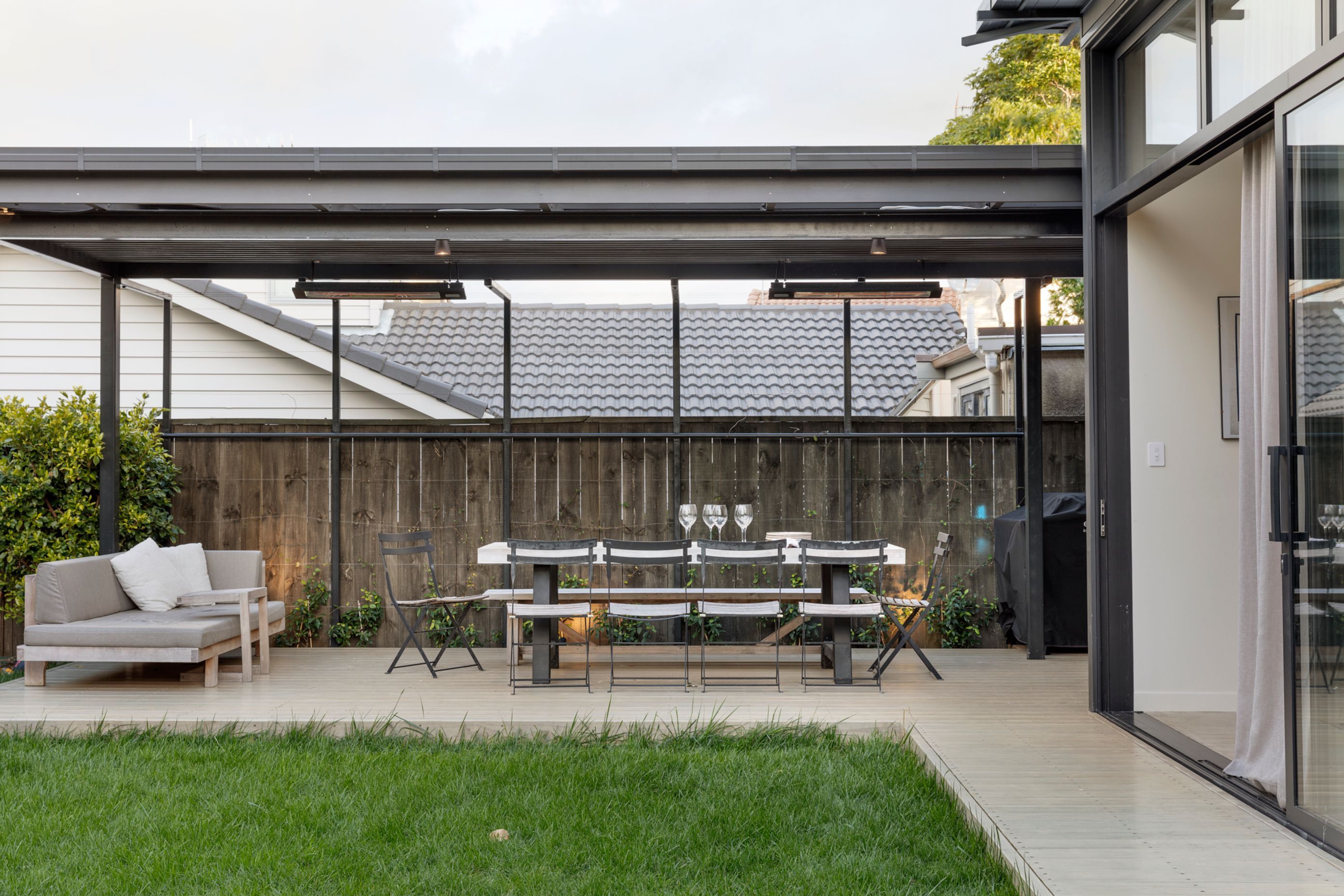 The dark-stained pergola provides a covered outdoor dining and lounge area off the indoor kitchen.