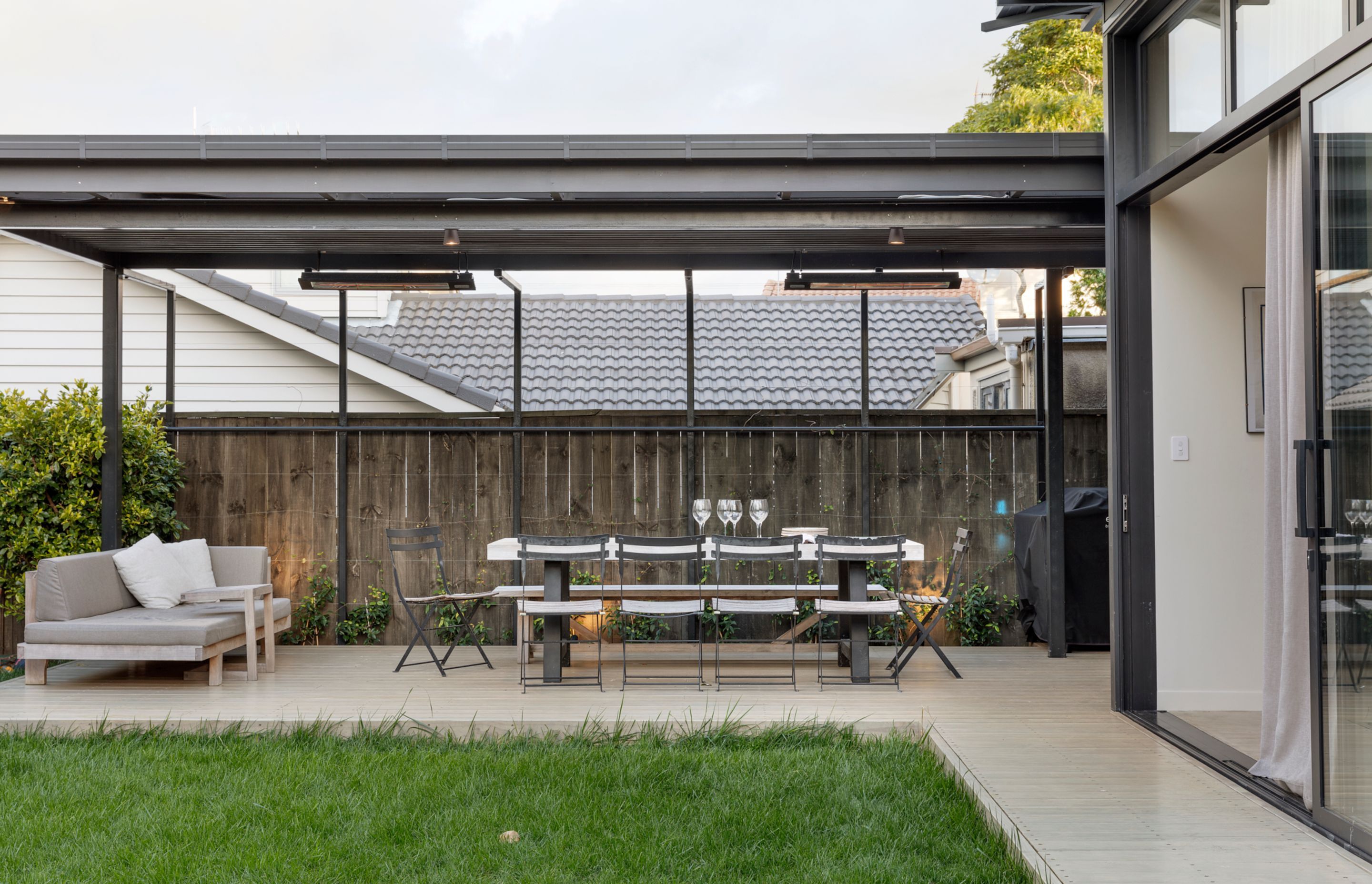 The dark-stained pergola provides a covered outdoor dining and lounge area off the indoor kitchen.