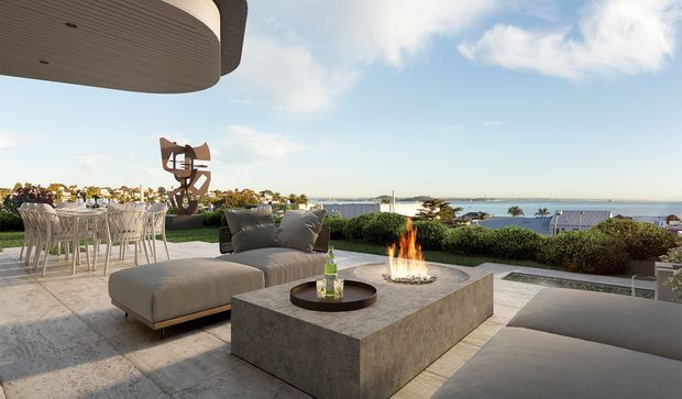 A sophisticated outdoor terrace overlooking a coastal waterfront, furnished with a large sectional-style lounge, sculptural dining chairs and table, and a substantial rectangular concrete fire table. The terrace has pale stone or concrete paving, low manicured hedges, a curved wood-lined overhead canopy, and a contemporary outdoor dining and lounge arrangement. A sculptural artwork and expansive ocean or harbour view are visible beyond the terrace.