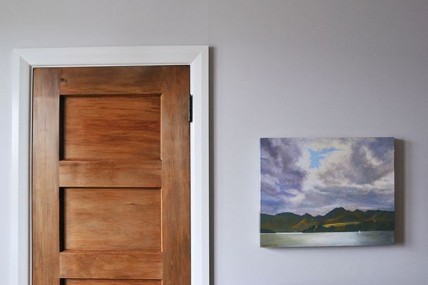 Close-up interior view of a traditional timber panel door set within white trim, beside a small landscape painting mounted on a pale grey wall. The image is focused on the doorway and wall surface, with no broader room context visible.