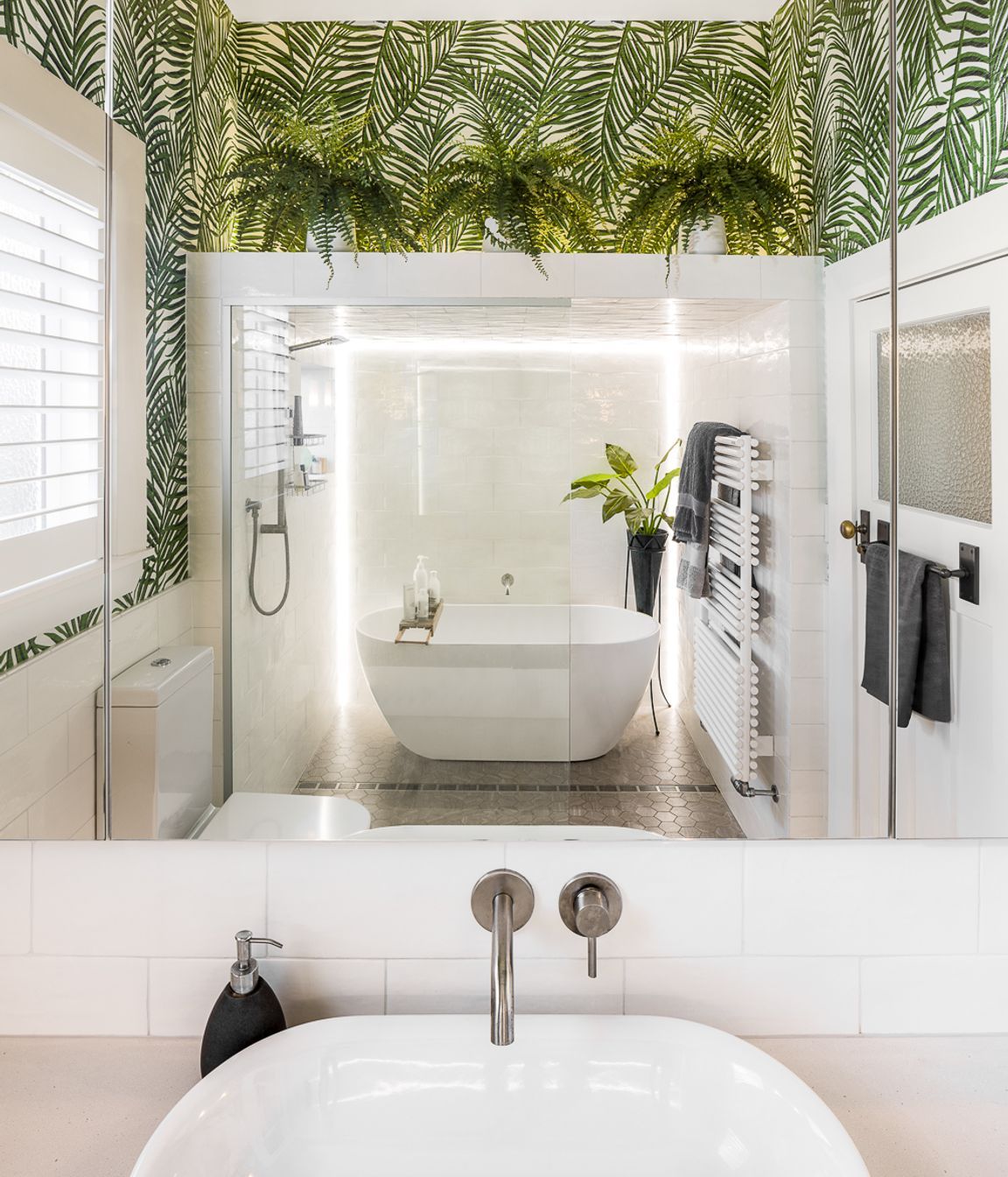 A neutral palette in the bathroom is invigorated with a wallpaper patterned with emerald green palms.