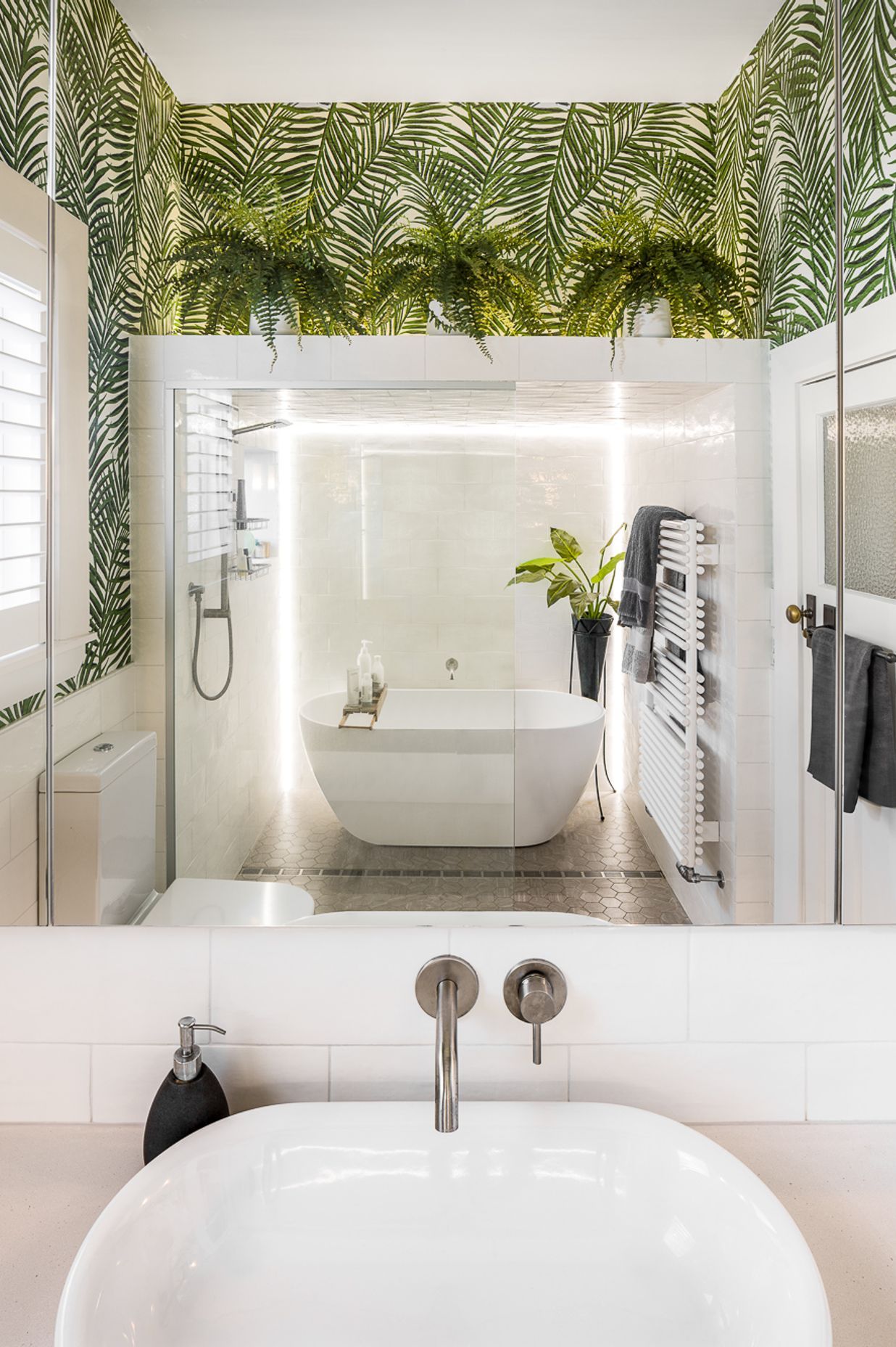 A neutral palette in the bathroom is invigorated with a wallpaper patterned with emerald green palms.