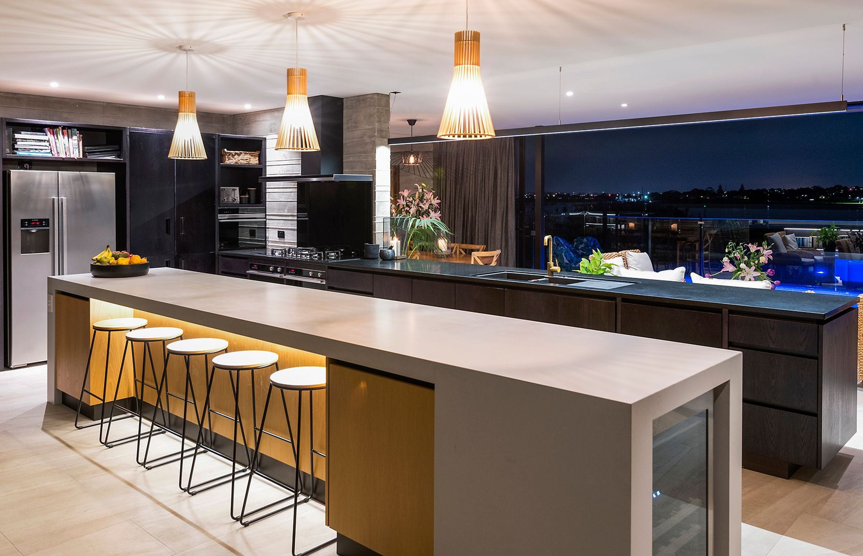 By night, the kitchen comes alive with feature lighting and a blue-lit pool as a backdrop.