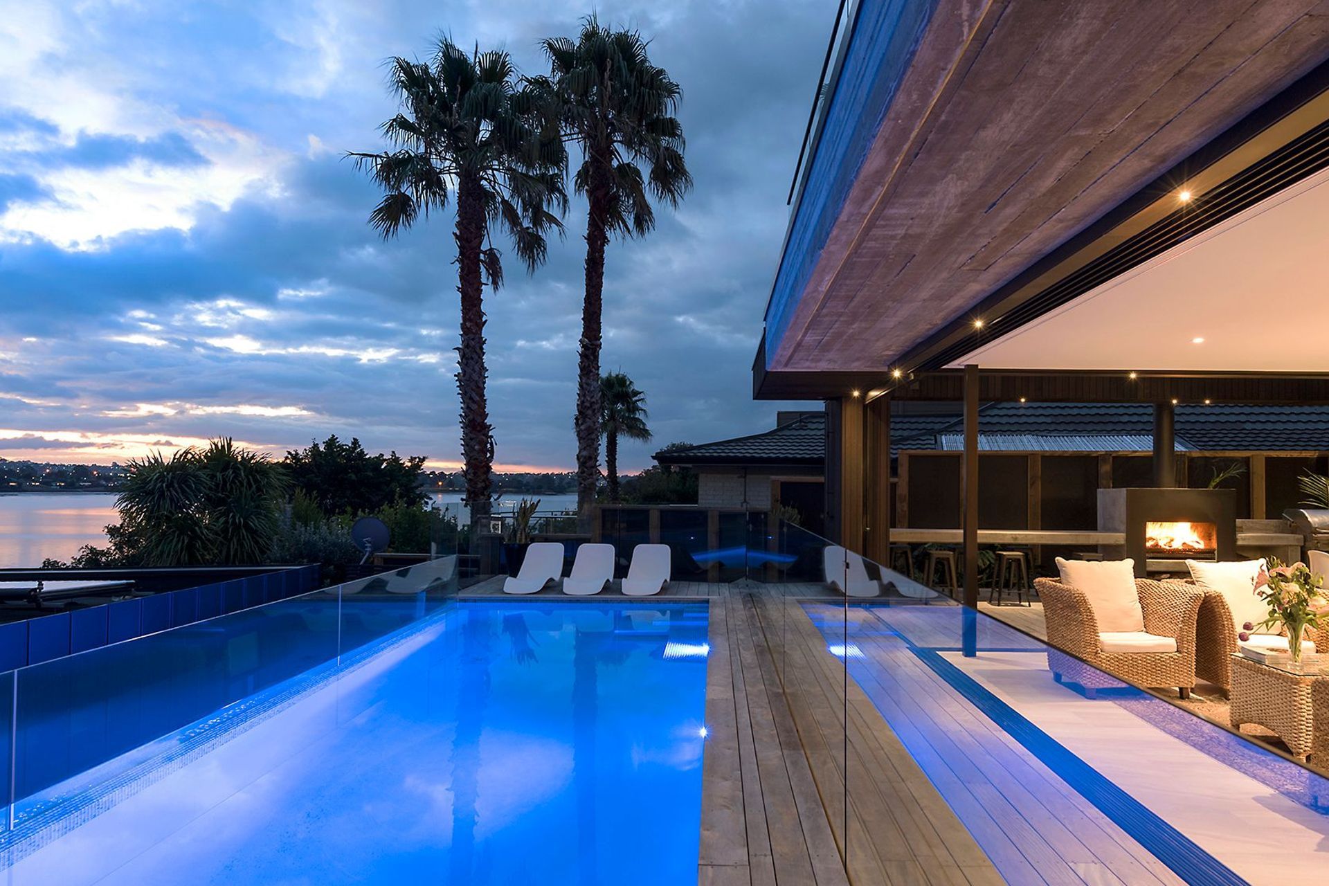 A night view of the blue-lit swimming pool gains a tropical feel from the shadows cast by mature palm trees and the setting sun.