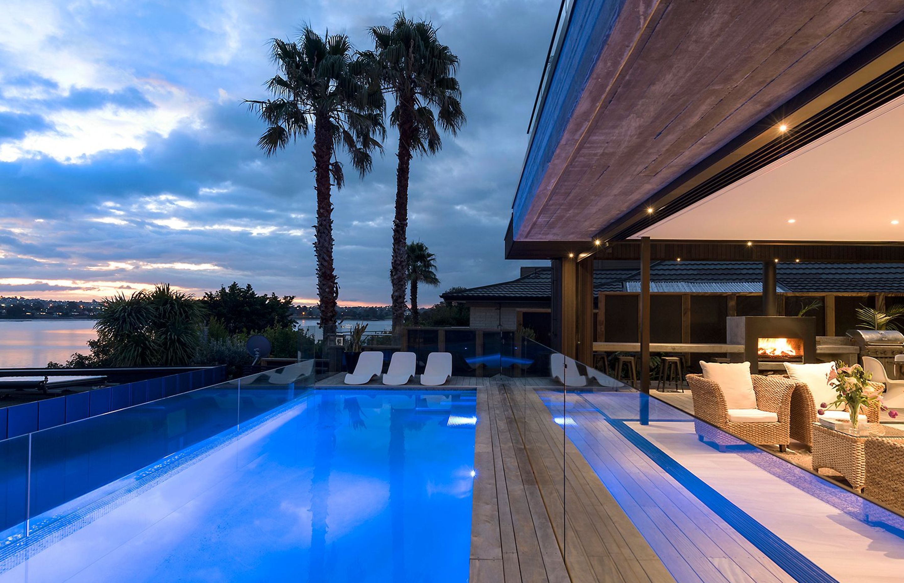 A night view of the blue-lit swimming pool gains a tropical feel from the shadows cast by mature palm trees and the setting sun.