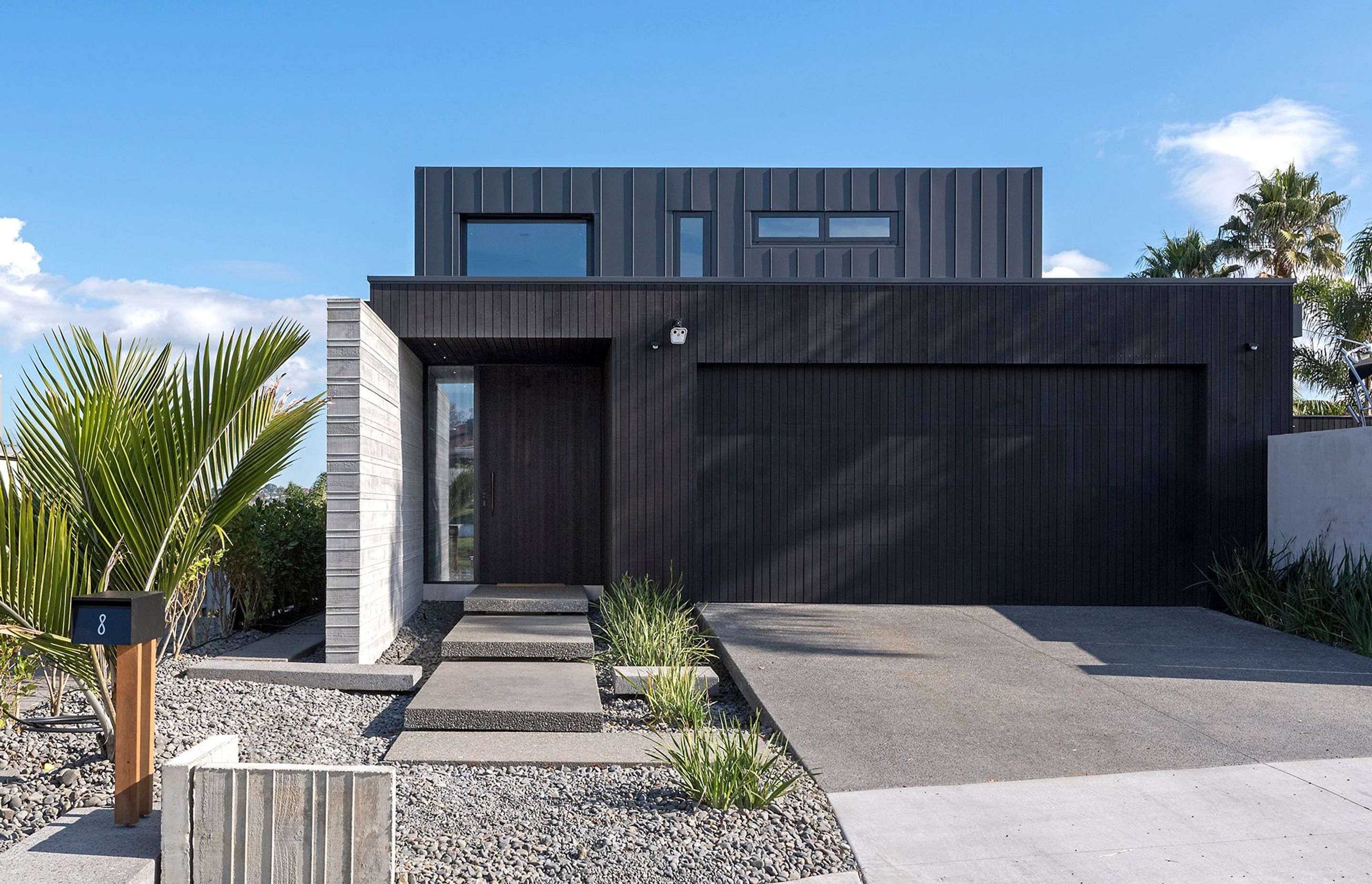 The streetview of Island Life in the Suburbs showing its distinctive dark-stained cedar and seamed metal claddings, complemented by a shuttered insitu concrete feature wall at the main entrance.