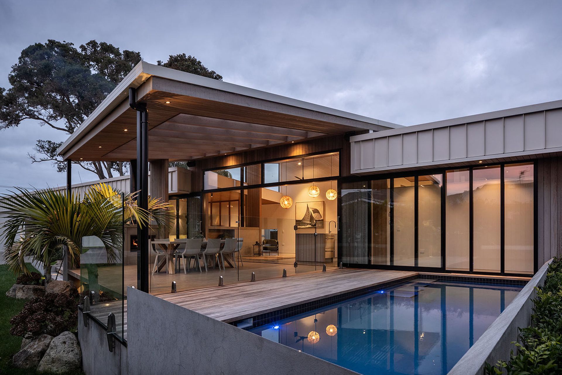 Next to the outdoor living area, the navy-tiled swimming pool is surrounded by decking. Two established pōhutukawa trees provide focal points at either end of the house.