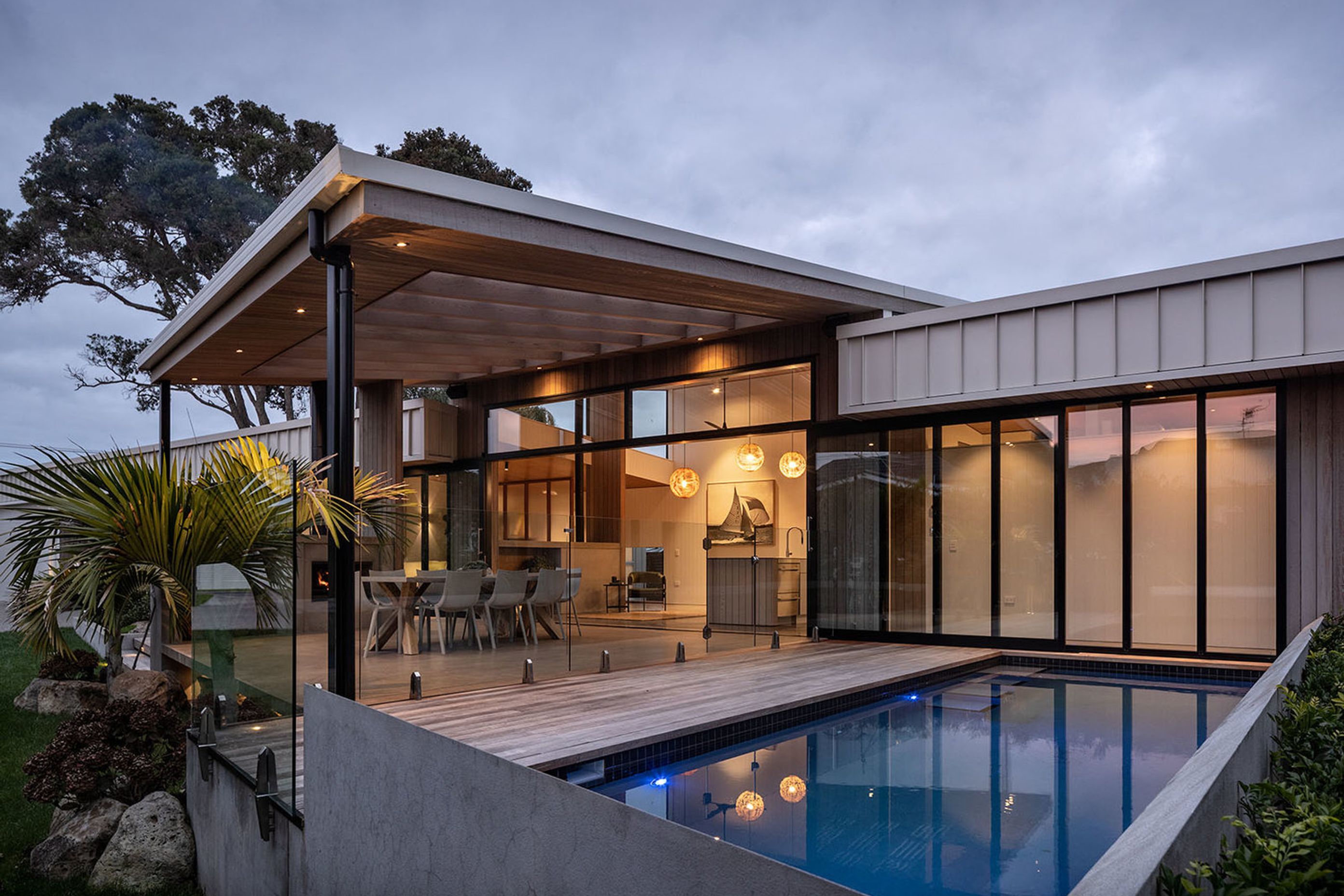 Next to the outdoor living area, the navy-tiled swimming pool is surrounded by decking. Two established pōhutukawa trees provide focal points at either end of the house.