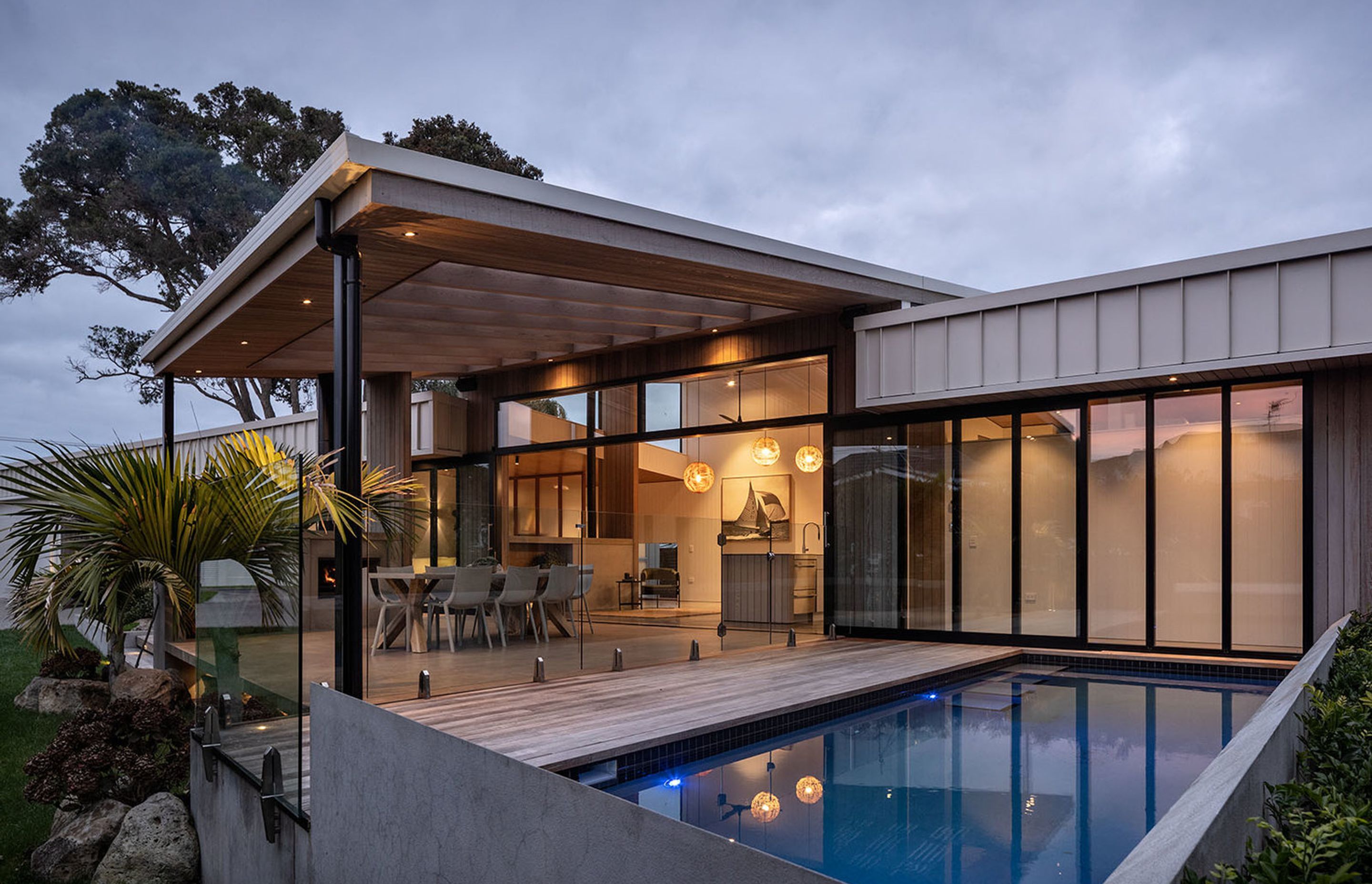 Next to the outdoor living area, the navy-tiled swimming pool is surrounded by decking. Two established pōhutukawa trees provide focal points at either end of the house.