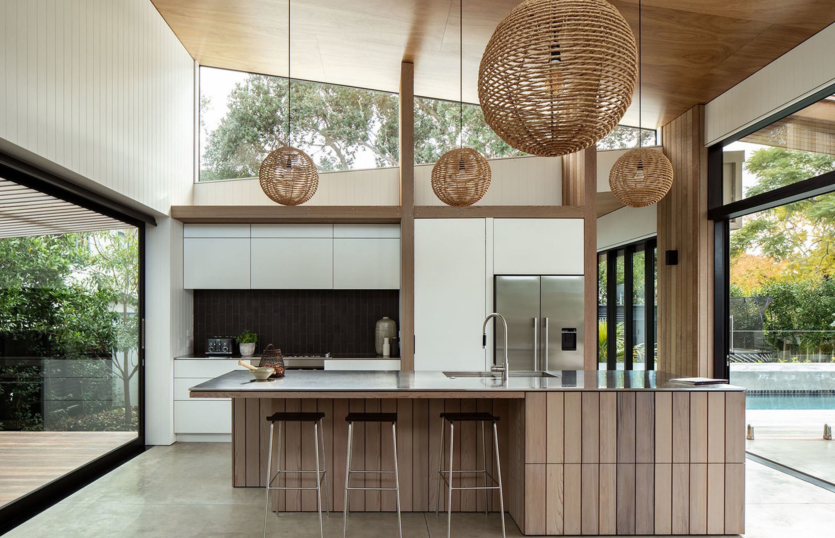 In the kitchen, high-level windows draw light deep into the home and provide a view of the old pōhutakawa tree. Sliding doors open the space up on either side.