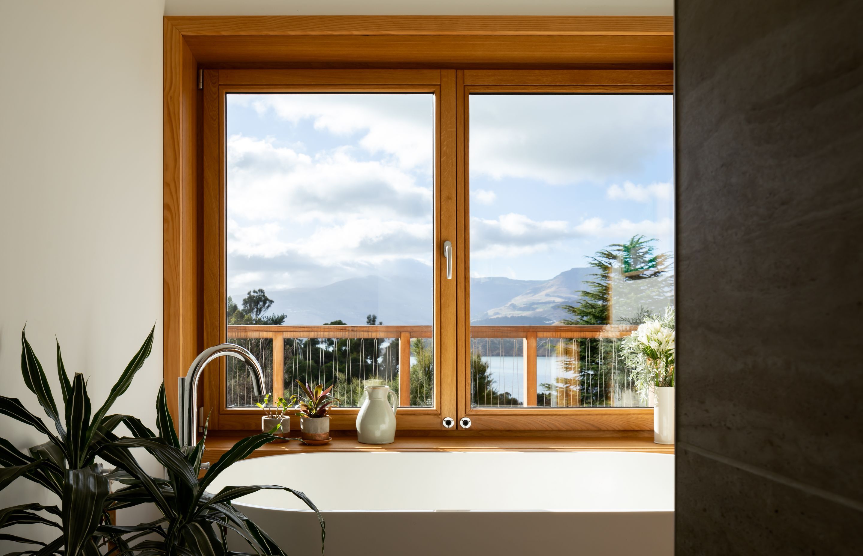 The timber window frames pop out of the house to create deep sills above a bathtub, highlighting the sensational view over Governors Bay.