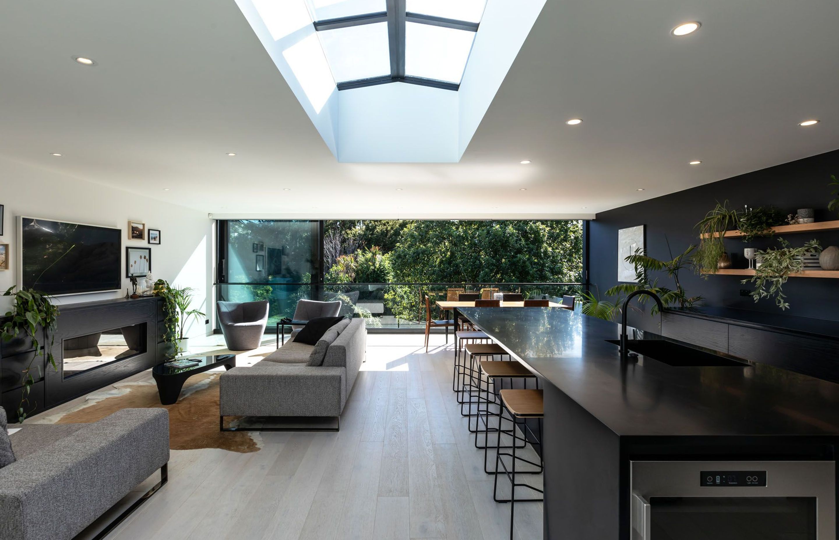 The open plan living area of the extension highlights the dichromatic colour scheme, punctuated with natural accents, to further reinforce the connection with nature through the sliding doors.