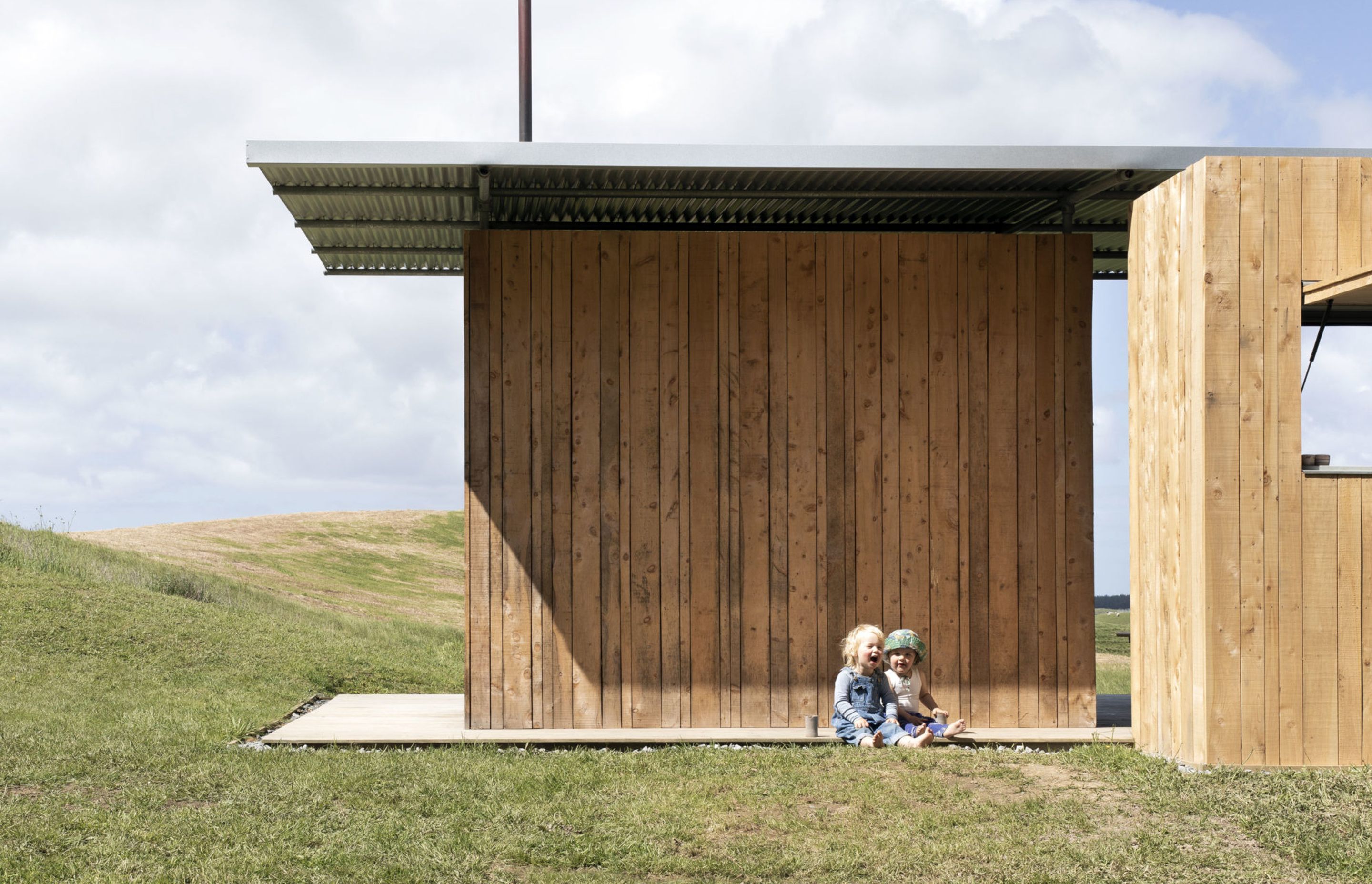 Two insulated macrocarpa-clad boxes sit beneath a classic Kiwi corrugated iron roof, creating a semi-sheltered space in between that encourages outdoor living.