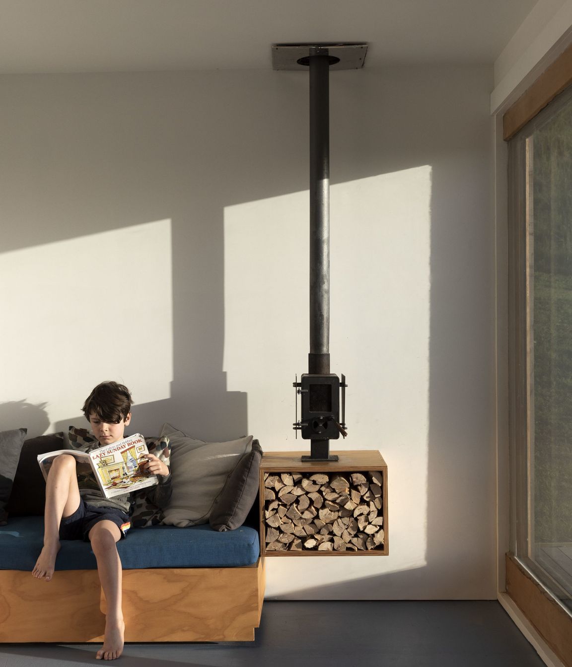 The owners's son enjoying some reading on the bespoke sofa, which features an adjacent fireplace and wood storage.
