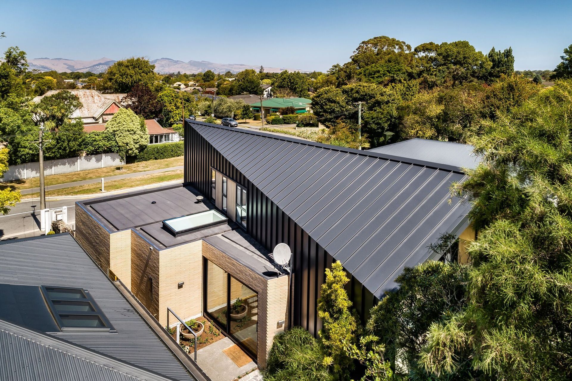 The folding roof of the metal form has a brick form jutting out the side containing the garage, a scullery (with skylight) and part of the kitchen opening up to a courtyard kitchen.