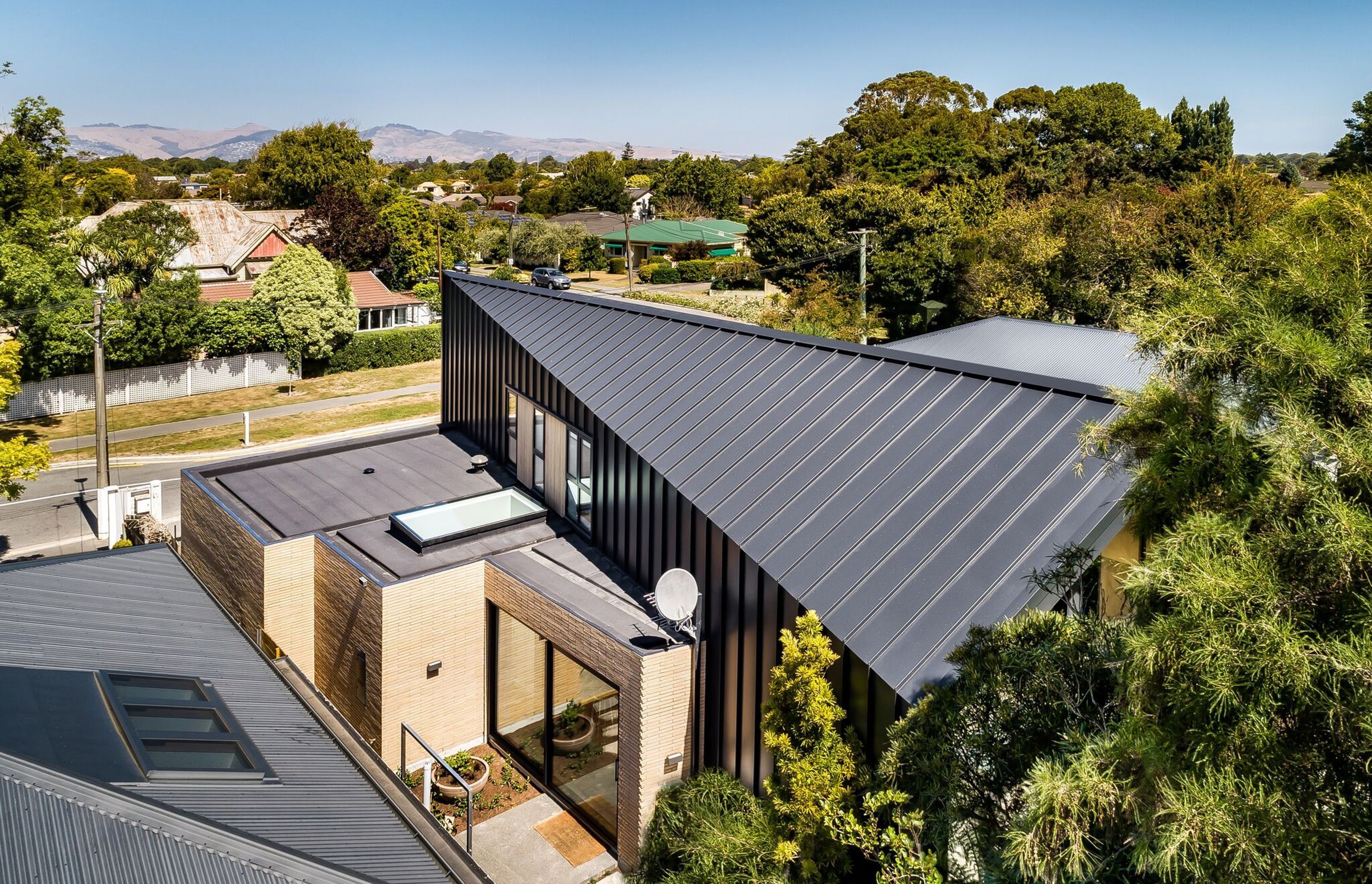 The folding roof of the metal form has a brick form jutting out the side containing the garage, a scullery (with skylight) and part of the kitchen opening up to a courtyard kitchen.