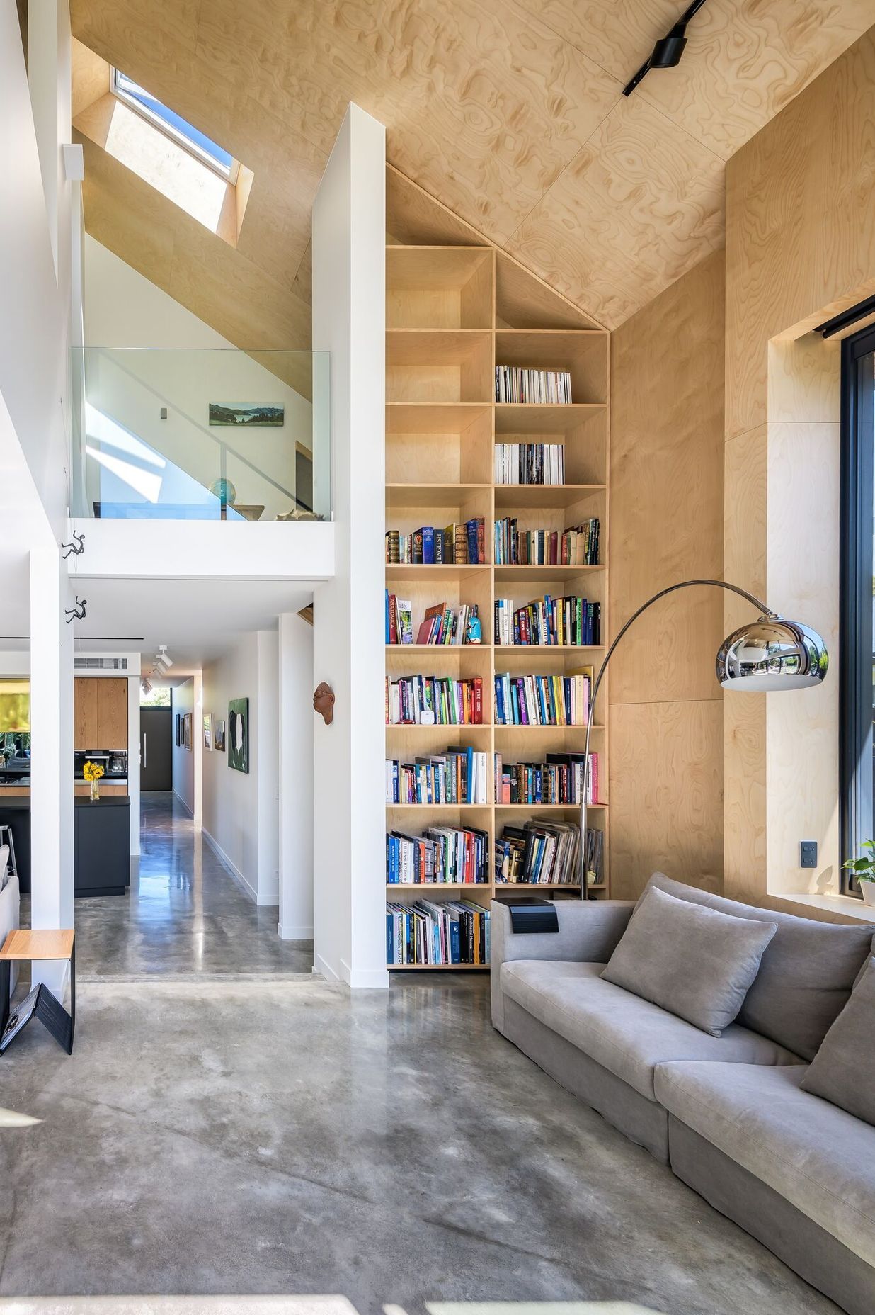 The double-height living space and bookcase leads south past the kitchen to the entry.