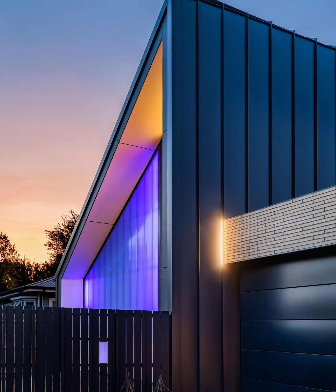 The street view shows the polycarbonate wall lit up at night and the flat metal wall of the half gable form. All photography by Anthony Turnham.
