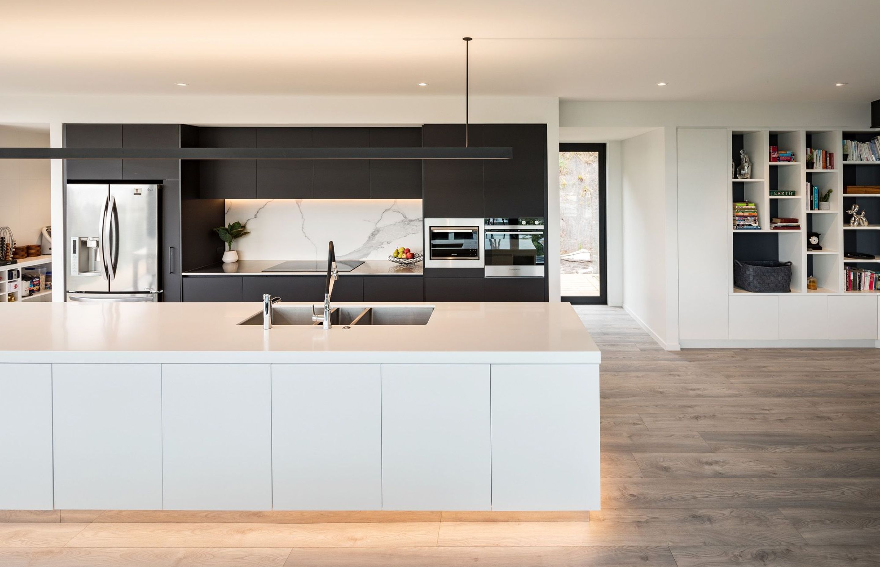 The kitchen is a monochromatic palette of black and white, offset by engineered oak flooring. Built-in joinery provides storage throughout the house, including the bookshelf above.