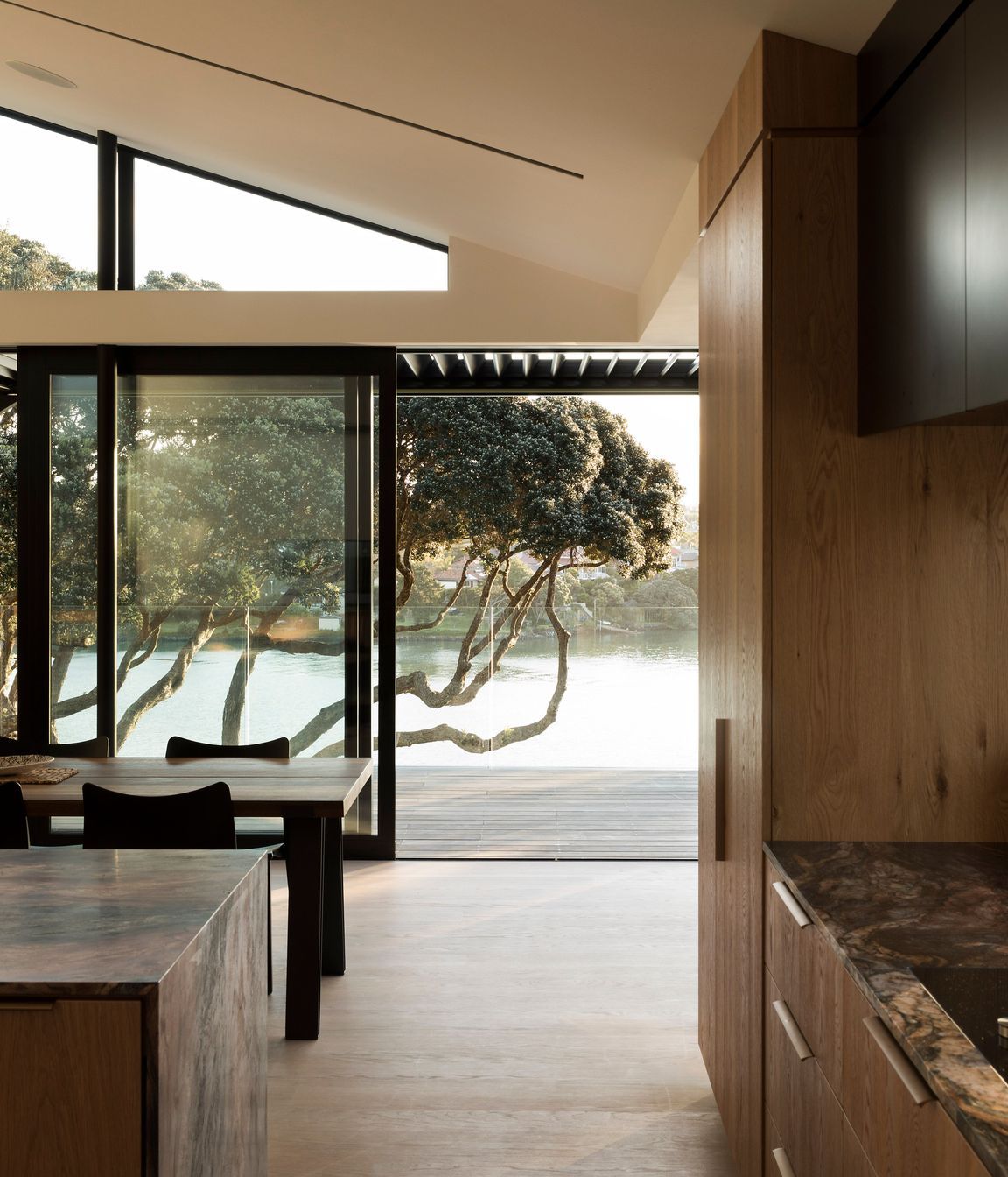 A view from the kitchen of pohutukawa trees and water.