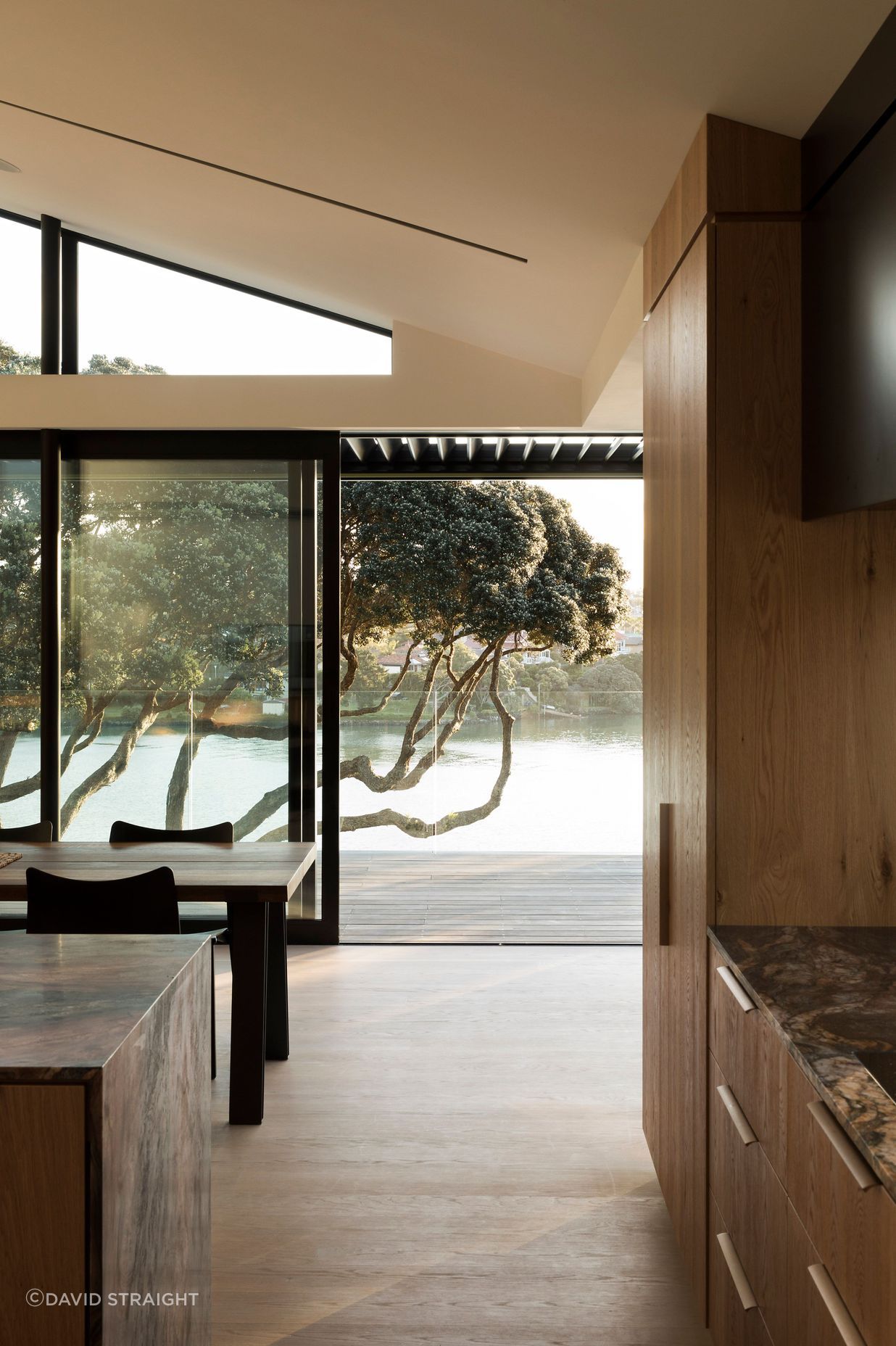 A view from the kitchen of pohutukawa trees and water.