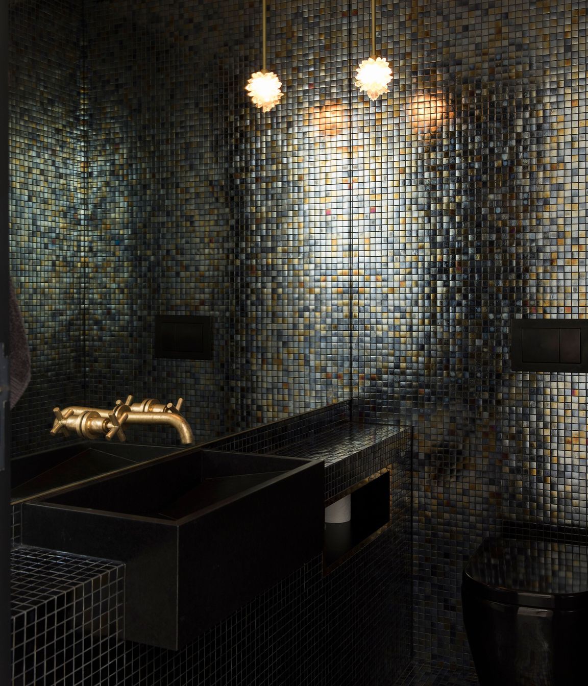 This dark and moody bathroom .features brass taps and black cabinetry.