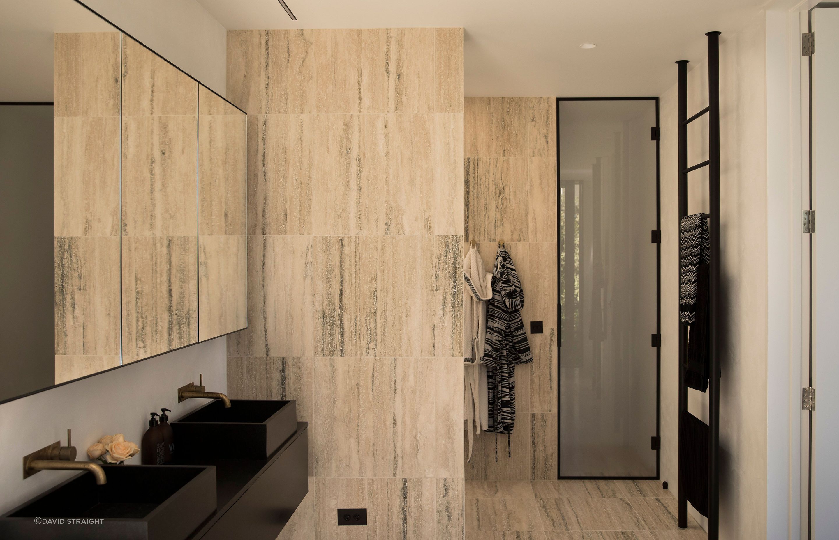 Light-coloured travertine stone tiles continue from the flooring onto the walls and cabinetry, creating a seamless high-quality finish.