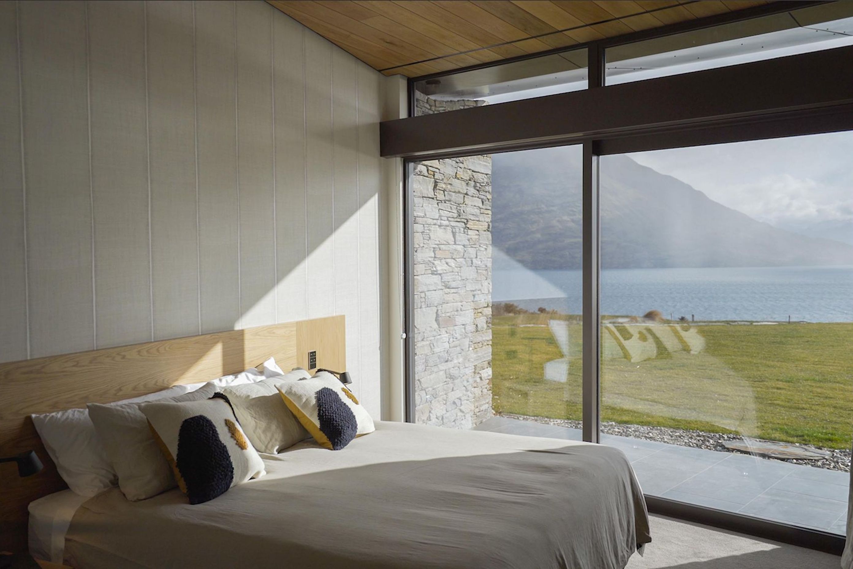 A bedroom on the lower floor has a calm neutral colour palette, making the most of the view of the lake and mountains. Photograph: ArchiPro.
