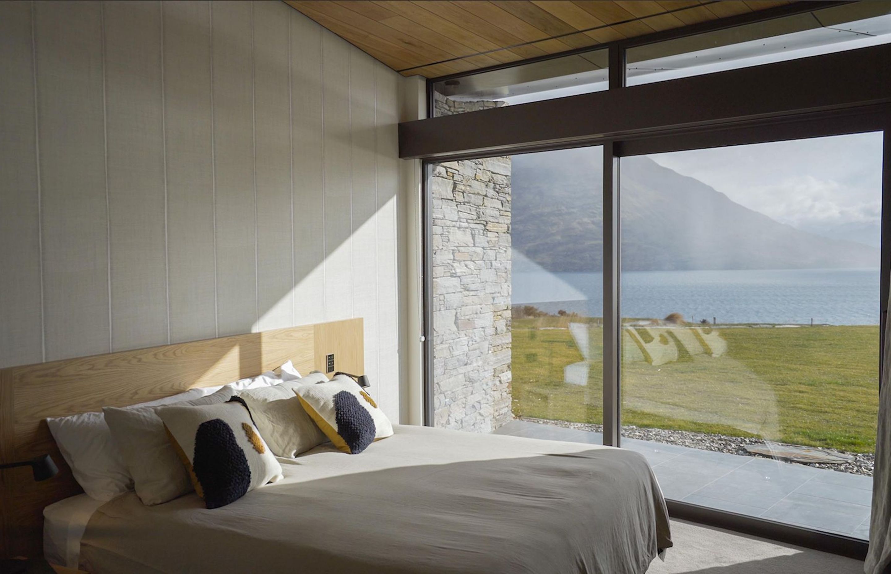 A bedroom on the lower floor has a calm neutral colour palette, making the most of the view of the lake and mountains. Photograph: ArchiPro.