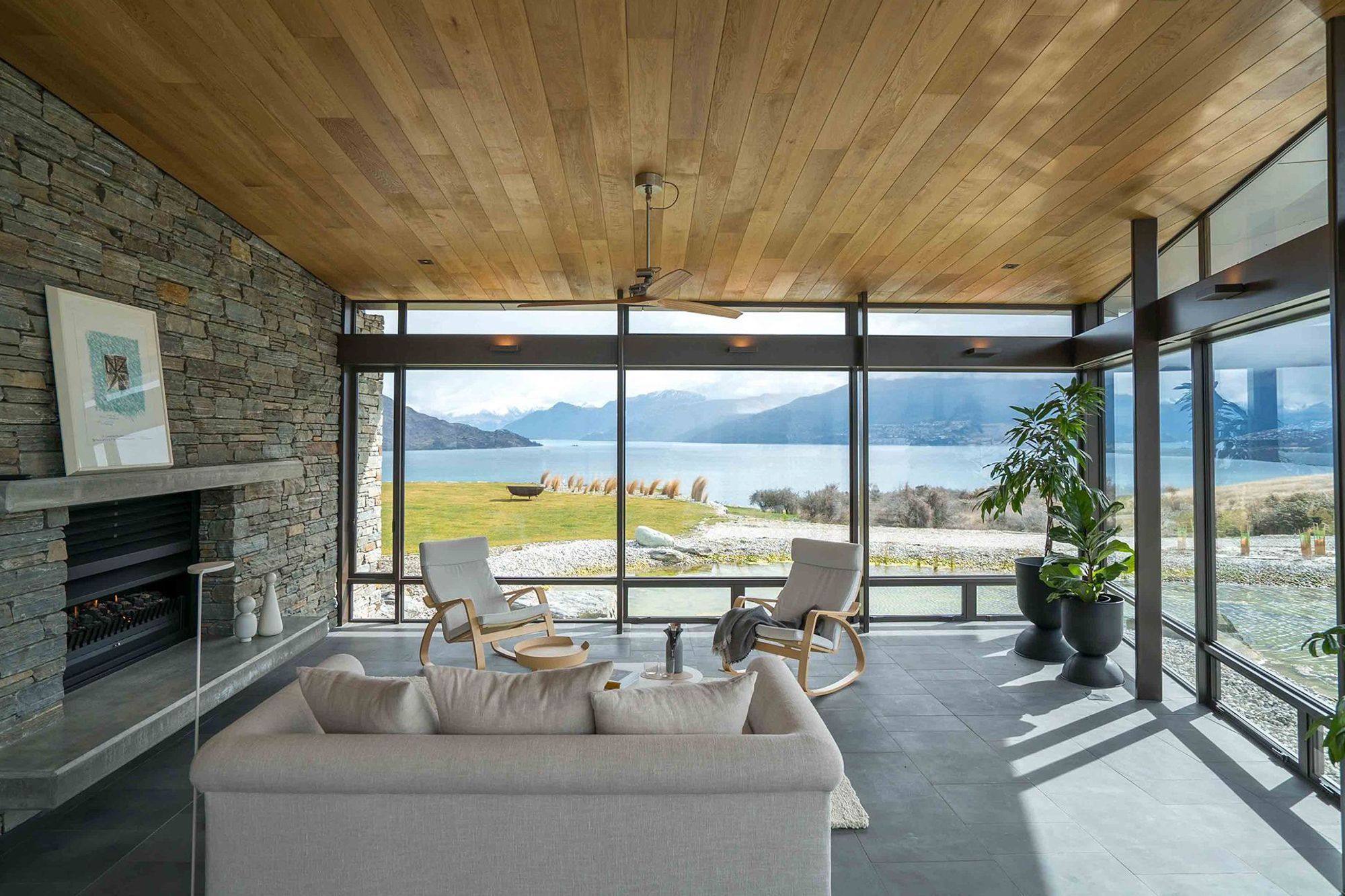 A second lounge area appears to float over the refection pond. A double-sided schist fireplace warms up the spacious open-plan living areas. Photograph: ArchiPro.