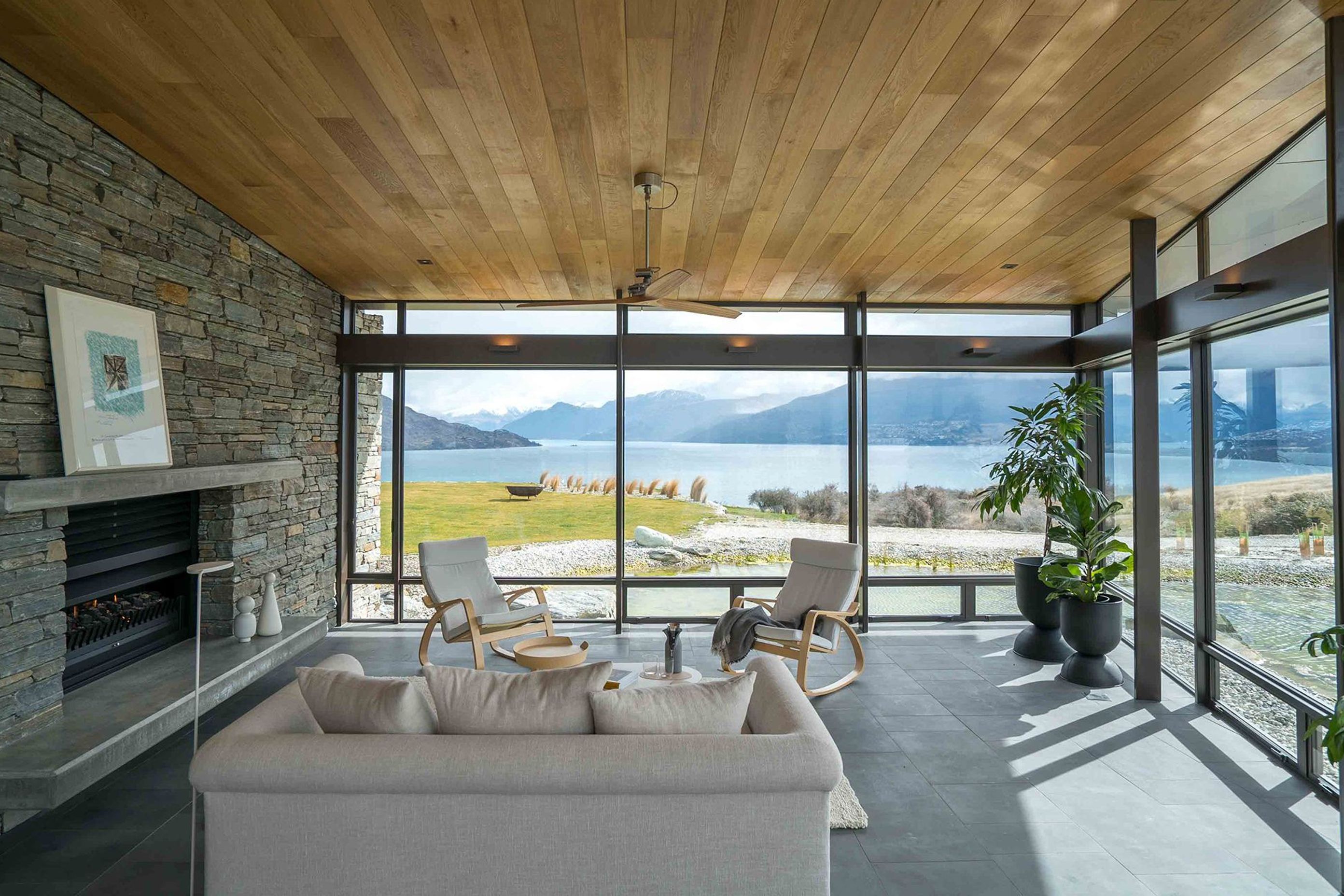 A second lounge area appears to float over the refection pond. A double-sided schist fireplace warms up the spacious open-plan living areas. Photograph: ArchiPro.