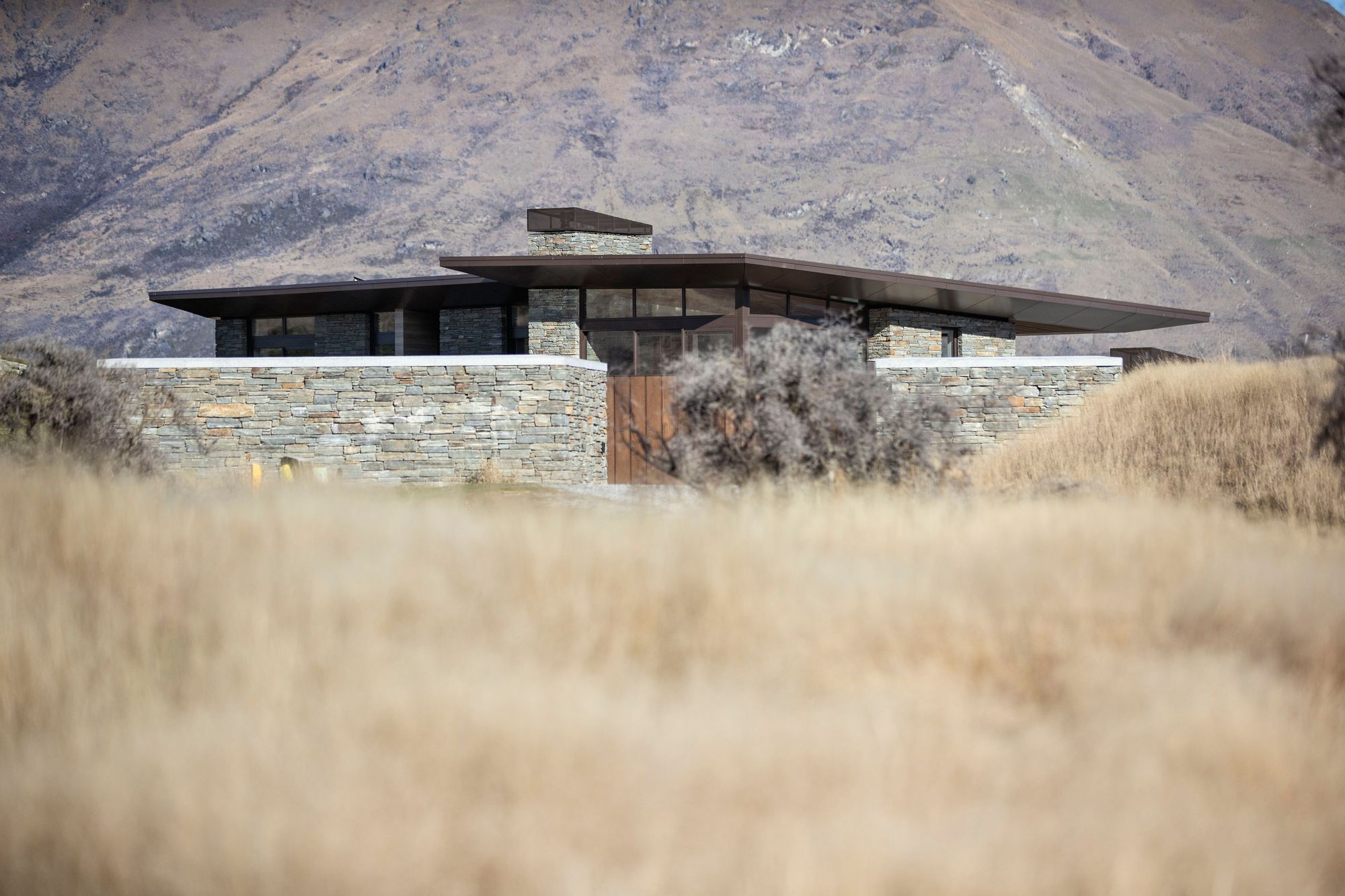 A low form, bronze aluminum joinery, cedar cladding and local schist help to blend the house into the surrounding tussock grasslands and rocky outcrops on the 1.272-hectare site. SD