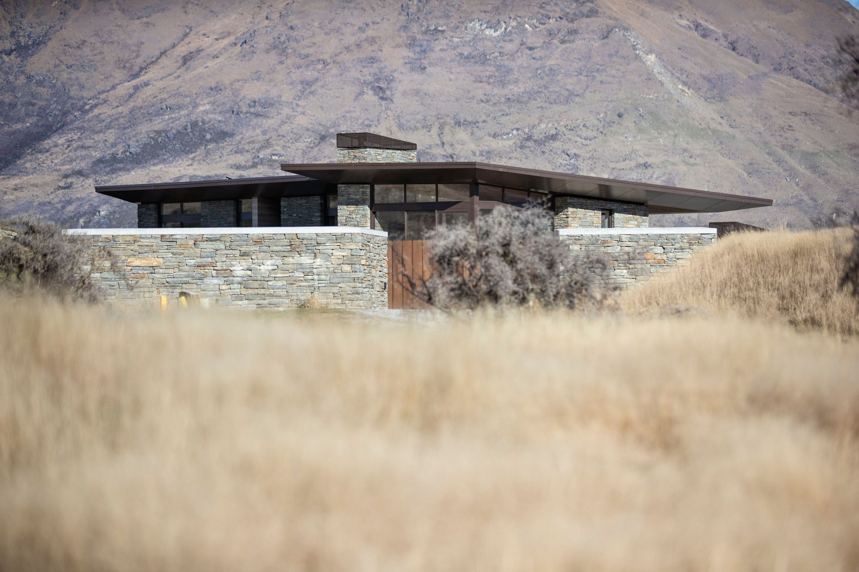 A low form, bronze aluminum joinery, cedar cladding and local schist help to blend the house into the surrounding tussock grasslands and rocky outcrops on the 1.272-hectare site. SD