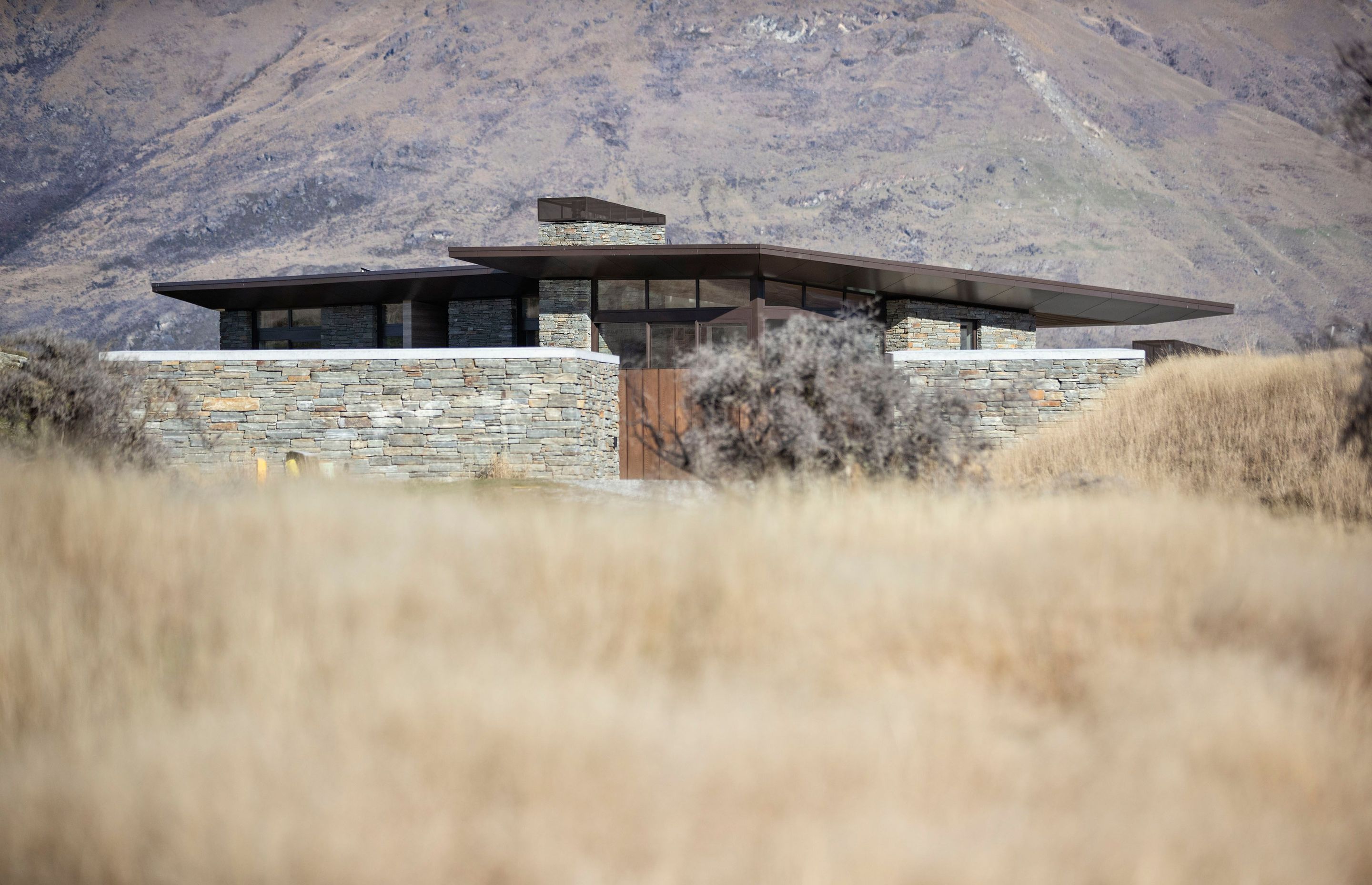 A low form, bronze aluminum joinery, cedar cladding and local schist help to blend the house into the surrounding tussock grasslands and rocky outcrops on the 1.272-hectare site. SD