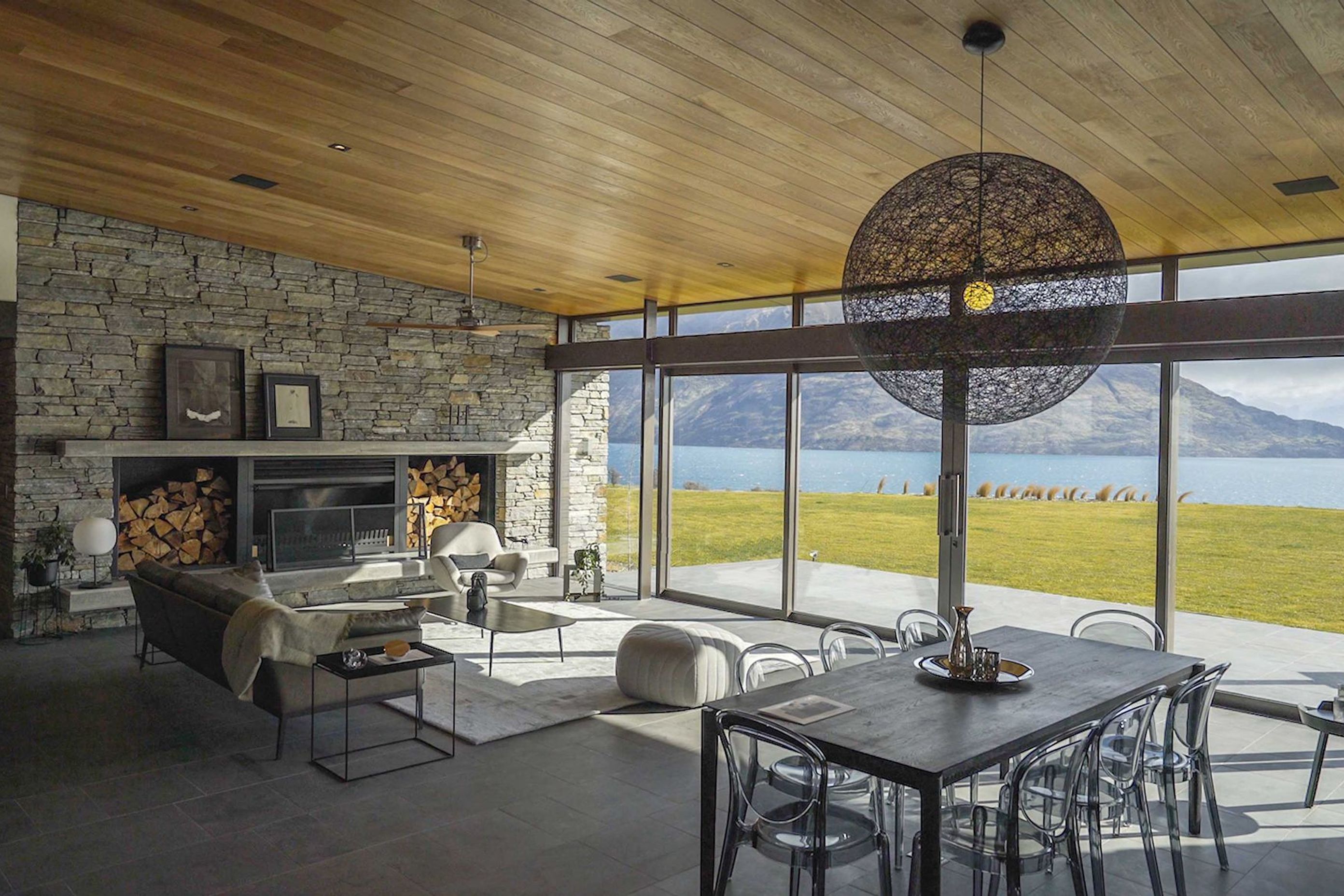 The dining and living area looks out to Lake Wakatipu. A natural palette of schist, timber and stone helps to blend the interior in with the surrounding landscape. AP.