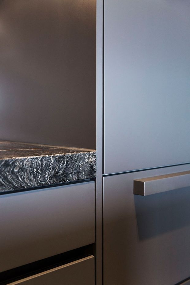 Close-up detail of dark contemporary built-in cabinetry with sleek handleless drawer fronts and a projecting rectangular handle. A dramatically veined dark stone benchtop or shelf runs across the left side, contrasting with smooth grey cabinetry panels and dark shadow gaps.