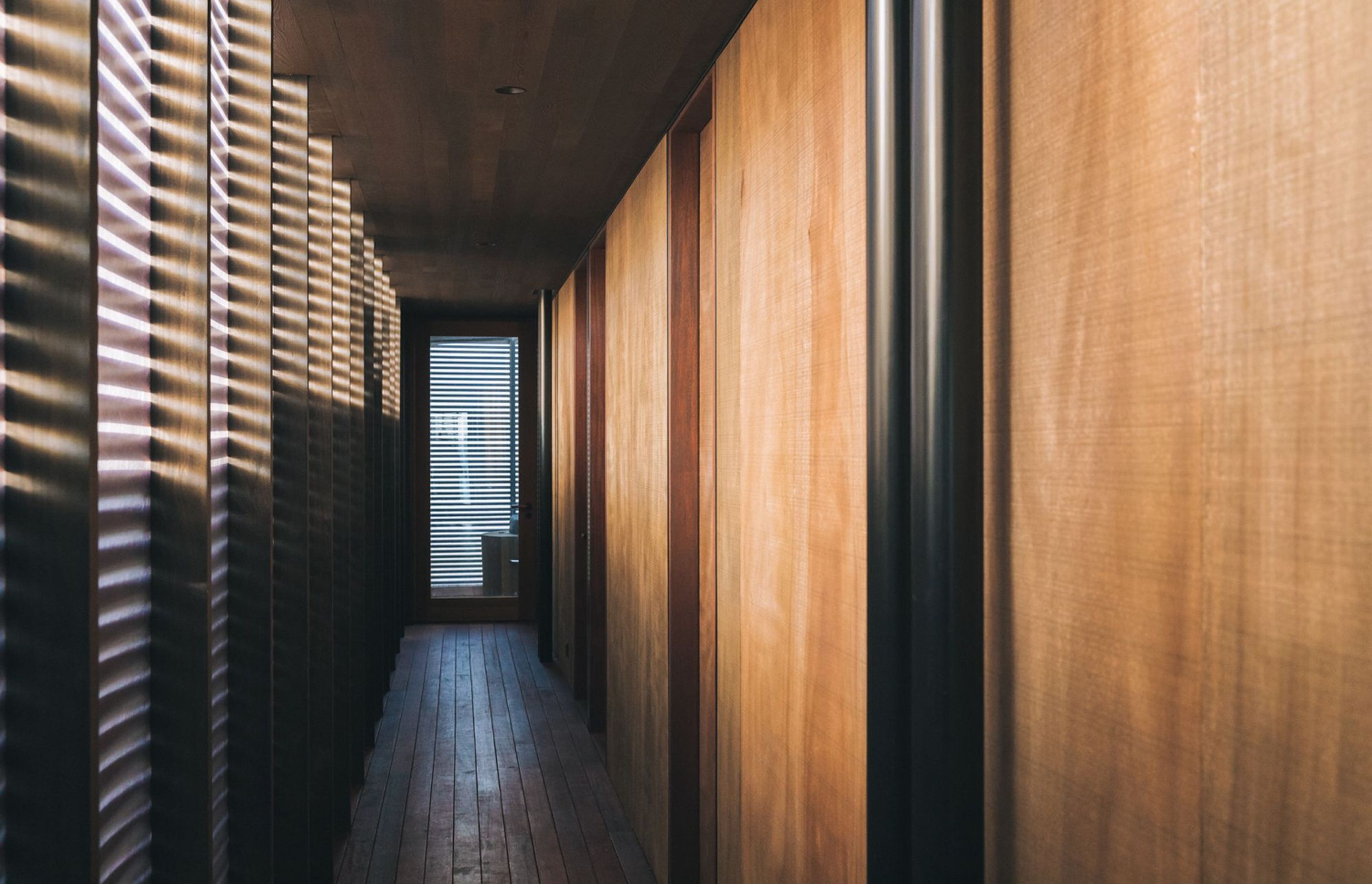 The internal hallway is actually classed as an outdoor space, with flooring of kwila decking and a simple perspex wall with cedar batons running across it.