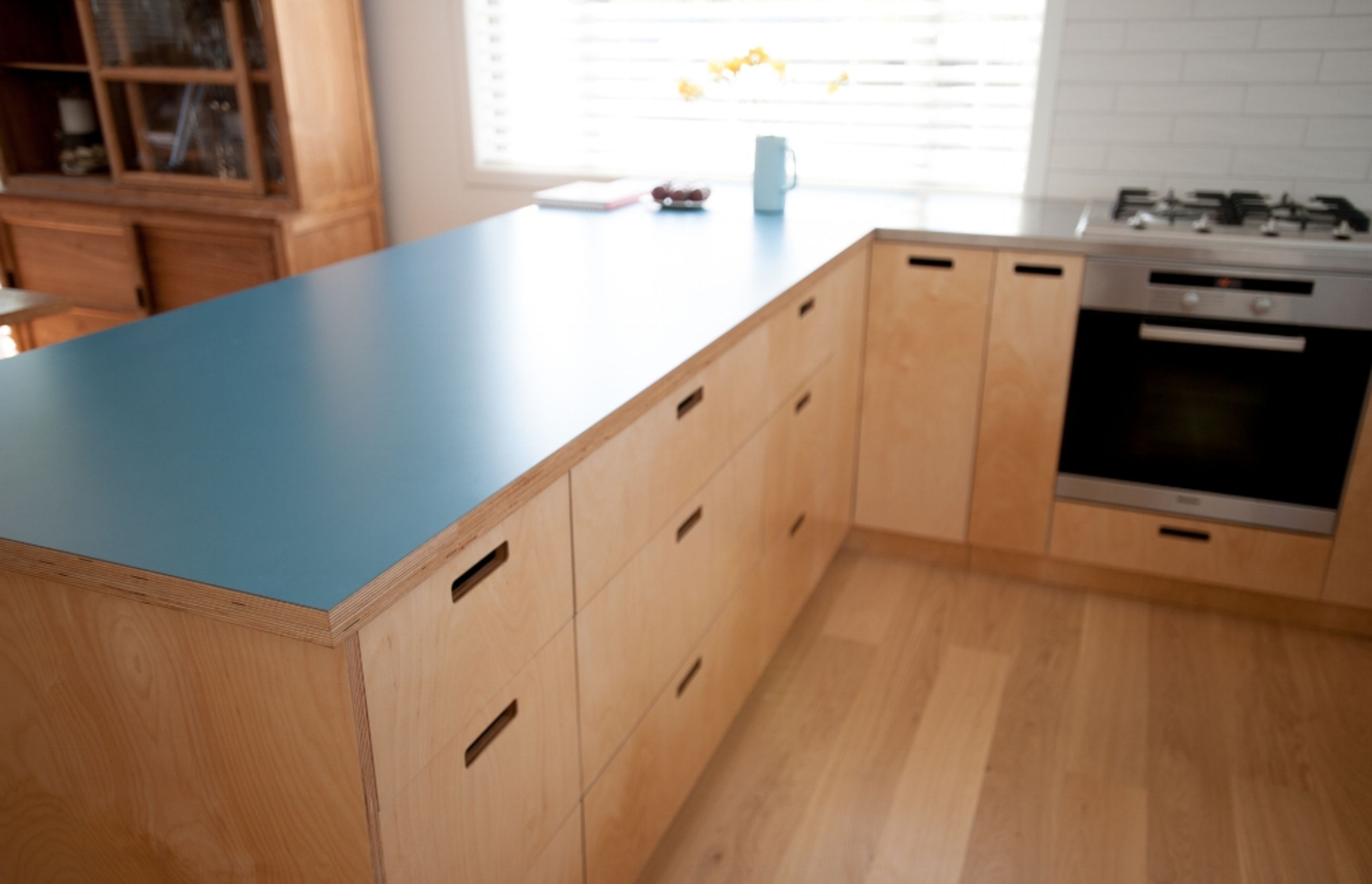 Clear lacquered Birch plywood fronts and spray finished pantry doors compliment a stainless steel bench top and laminated Birch plywood breakfast bar.