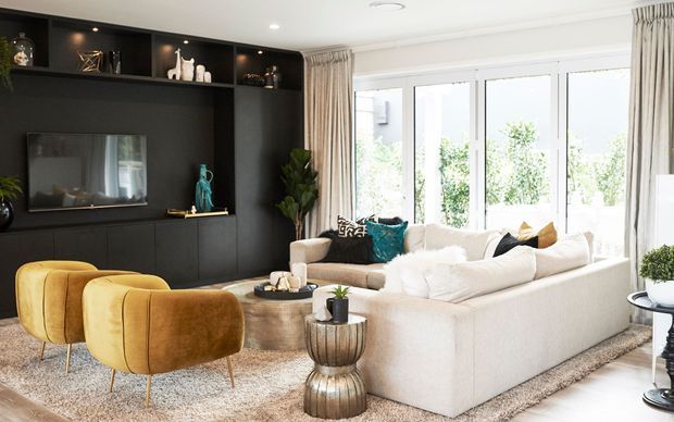 Bright, refined living room with a large cream sectional sofa, mustard velvet lounge chairs, textured rug, dark built-in media cabinetry, and full-height glazed doors framed by curtains. The room combines warm neutral furnishings with bold dark joinery and teal accents.