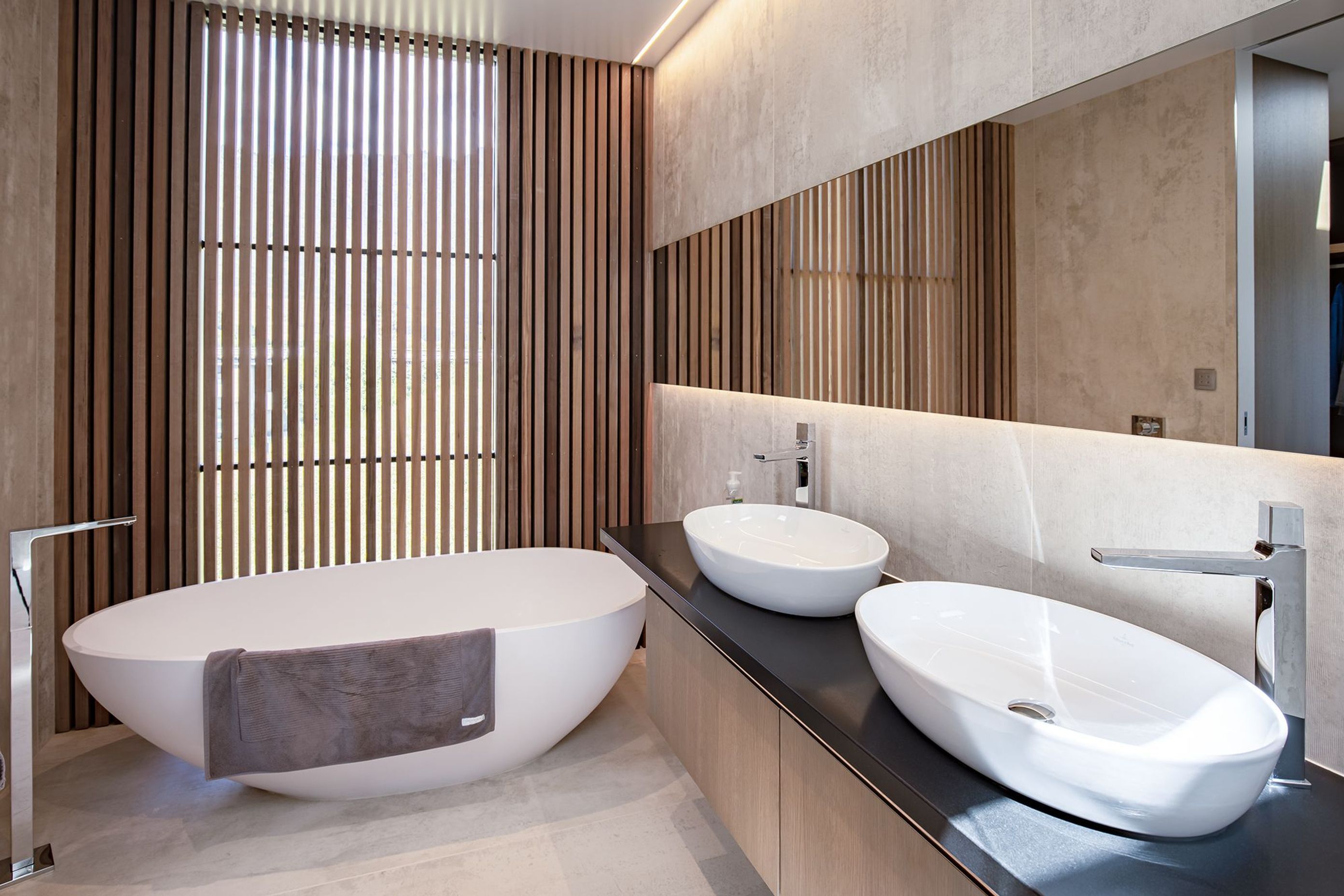 A curvaceous bath and sinks add another dimension to the sharp lines of the large-format tiling and the cedar screen.