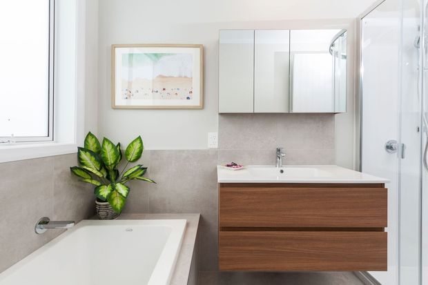 Bright contemporary bathroom featuring a white bathtub, floating dark-wood vanity with integrated basin, mirrored wall cabinet, tiled walls, glass shower enclosure, and a potted plant by the window.