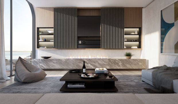 Refined contemporary living room with a built-in media wall, dark vertical timber battens, open display shelving, a large television, and a long marble-clad fireplace surround. A low dark coffee table sits centrally on a large rug, with sofas and a sculptural lounge chair framing the room. Full-height curved glazing on the left provides a bright coastal outlook.