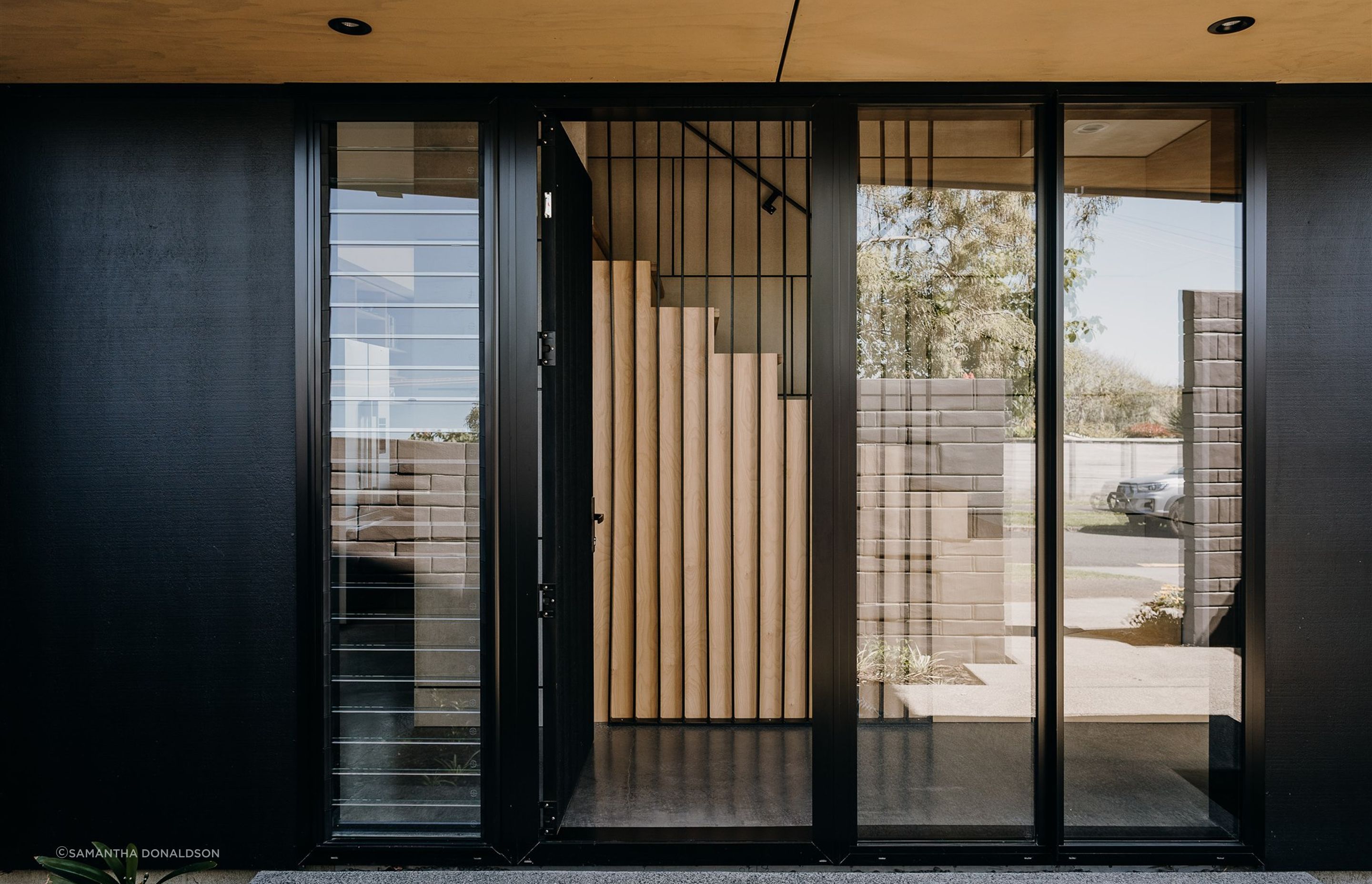 A floated concrete floor, black steel fins and a timber stair continue the material palette of the exterior.