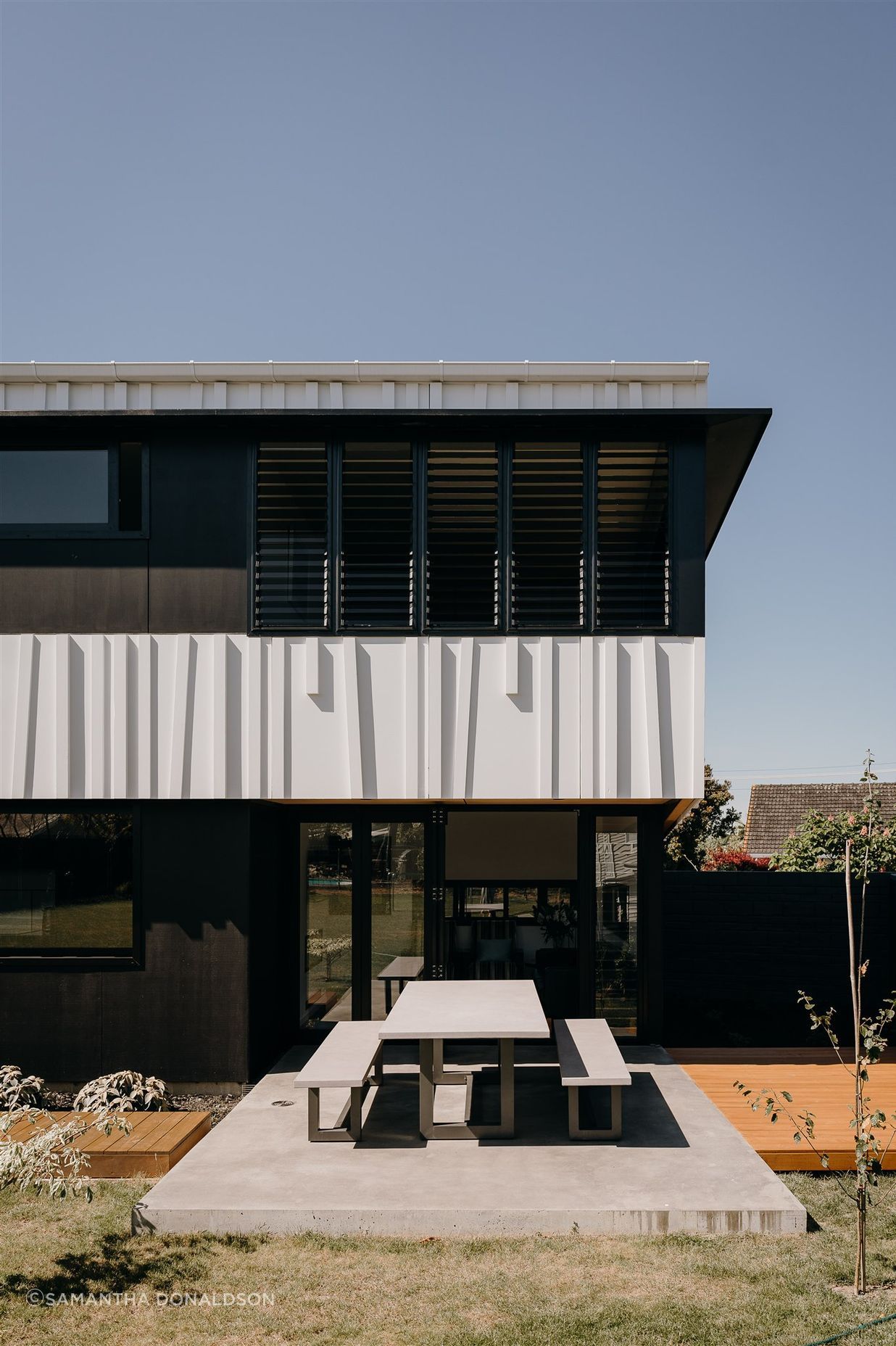 The main living area opens onto the private, rear backyard, whose central space is atop a concrete slab met on either side by timber decking that runs the length of this long, narrow house